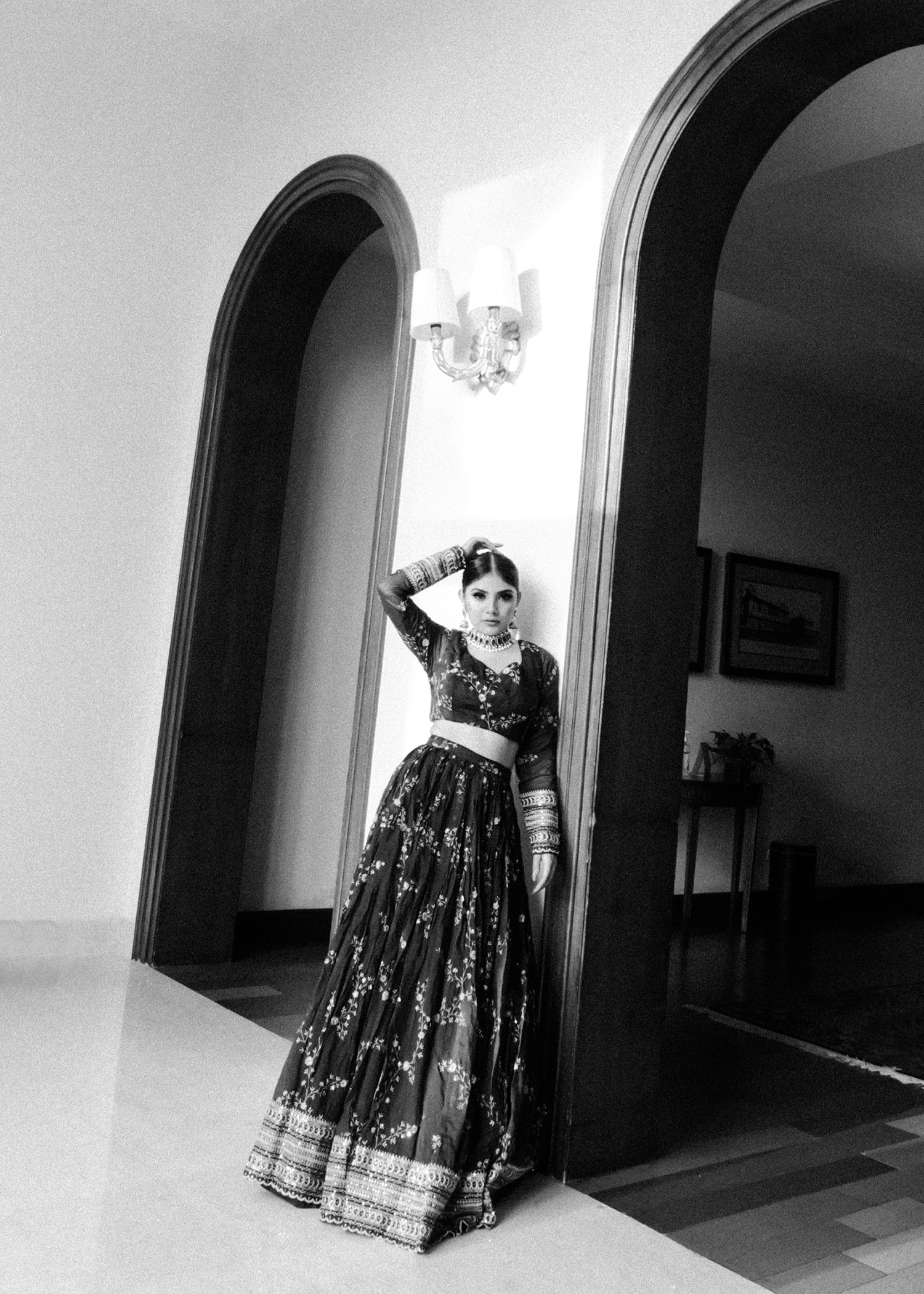 A black and white artistic photograph of a person in a long dress standing in an arched corridor with dramatic lighting.