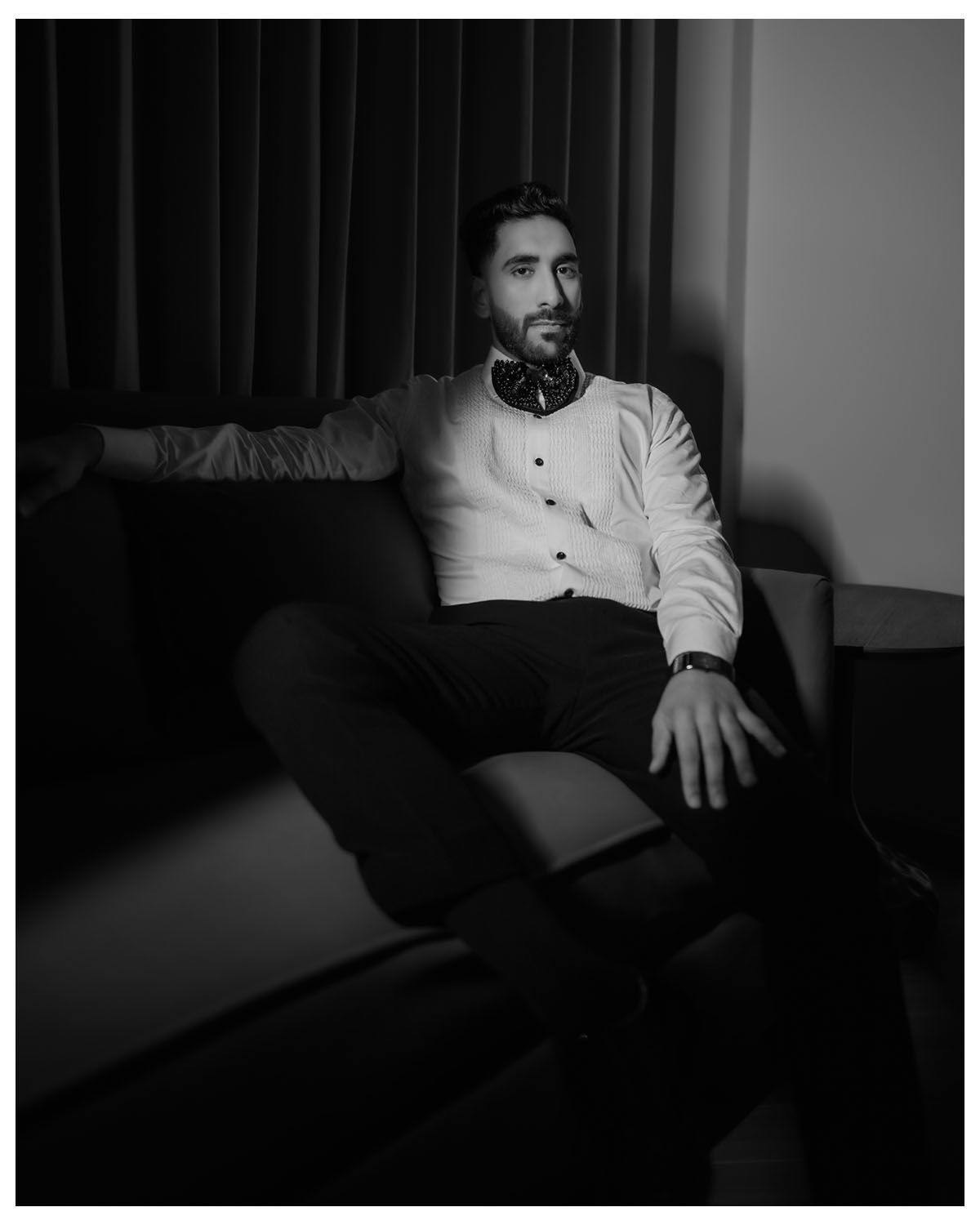 Black and white portrait of man in formal shirt relaxing on couch.