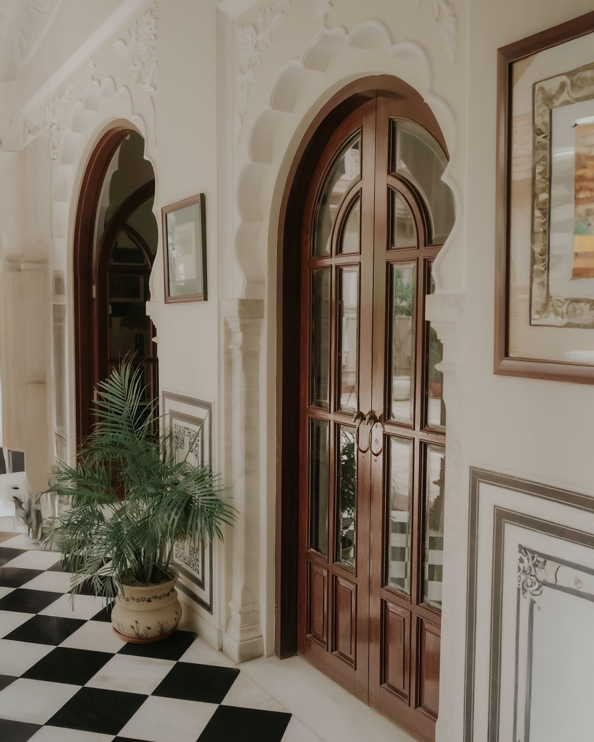 Interior corridor with checkered floor, wooden arched doors, and classic architectural details.