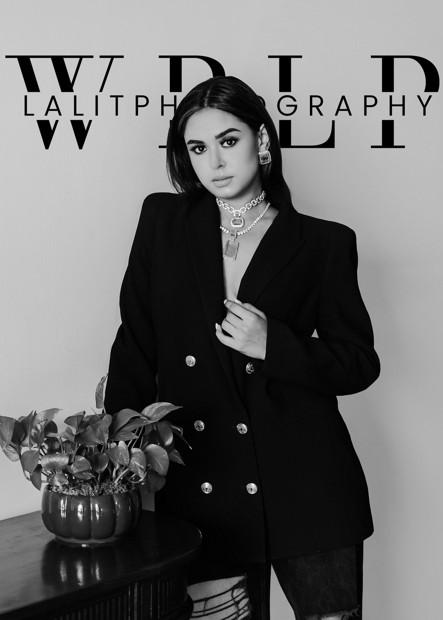 A black and white fashion photograph showing a model in a double-breasted blazer next to a potted plant.