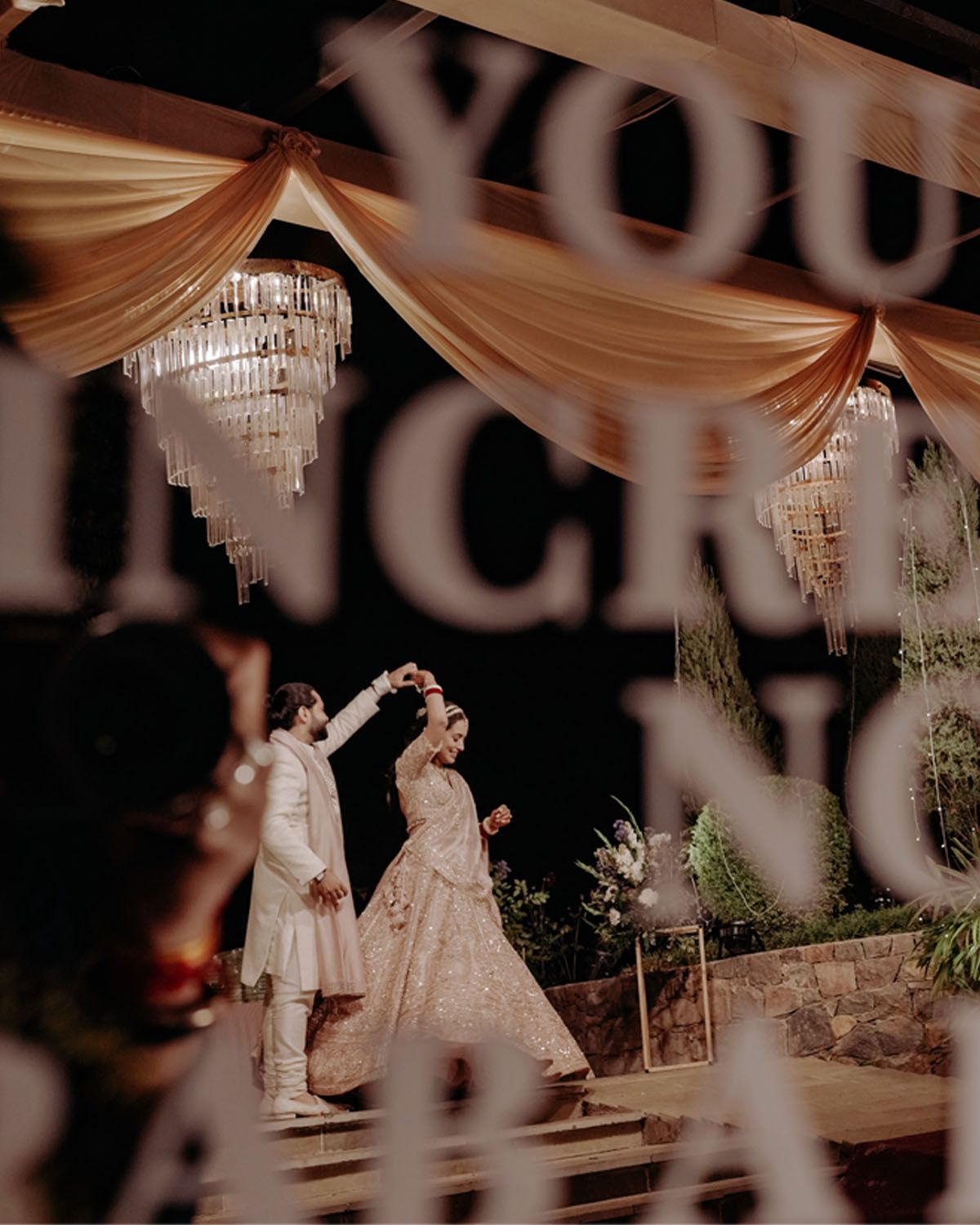 An elegantly decorated wedding venue with crystal chandeliers and draped fabric creates a romantic atmosphere during a reception.