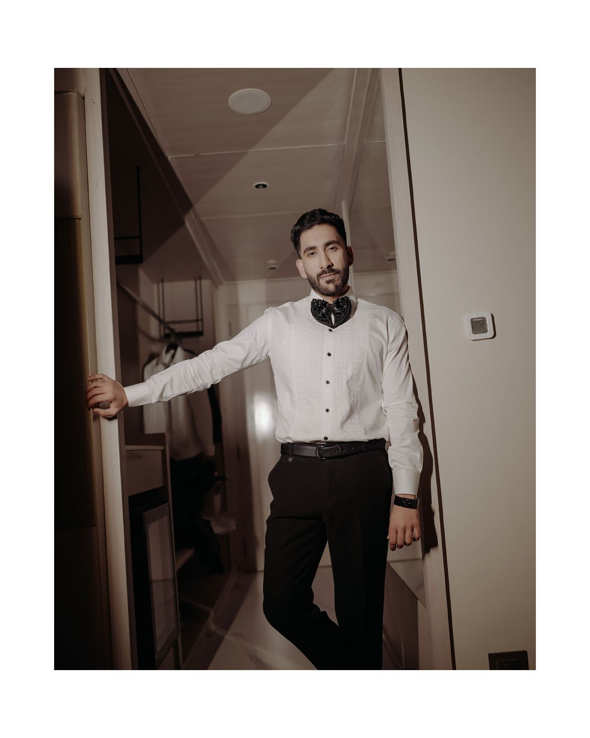 Person in white dress shirt and black pants poses elegantly in dimly lit hallway.
