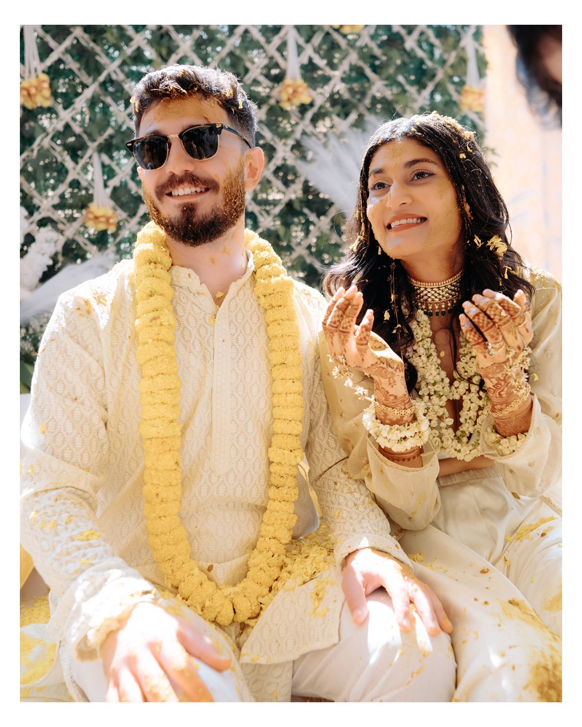 Guests in coordinated cream and yellow attire with traditional garlands at outdoor celebration.