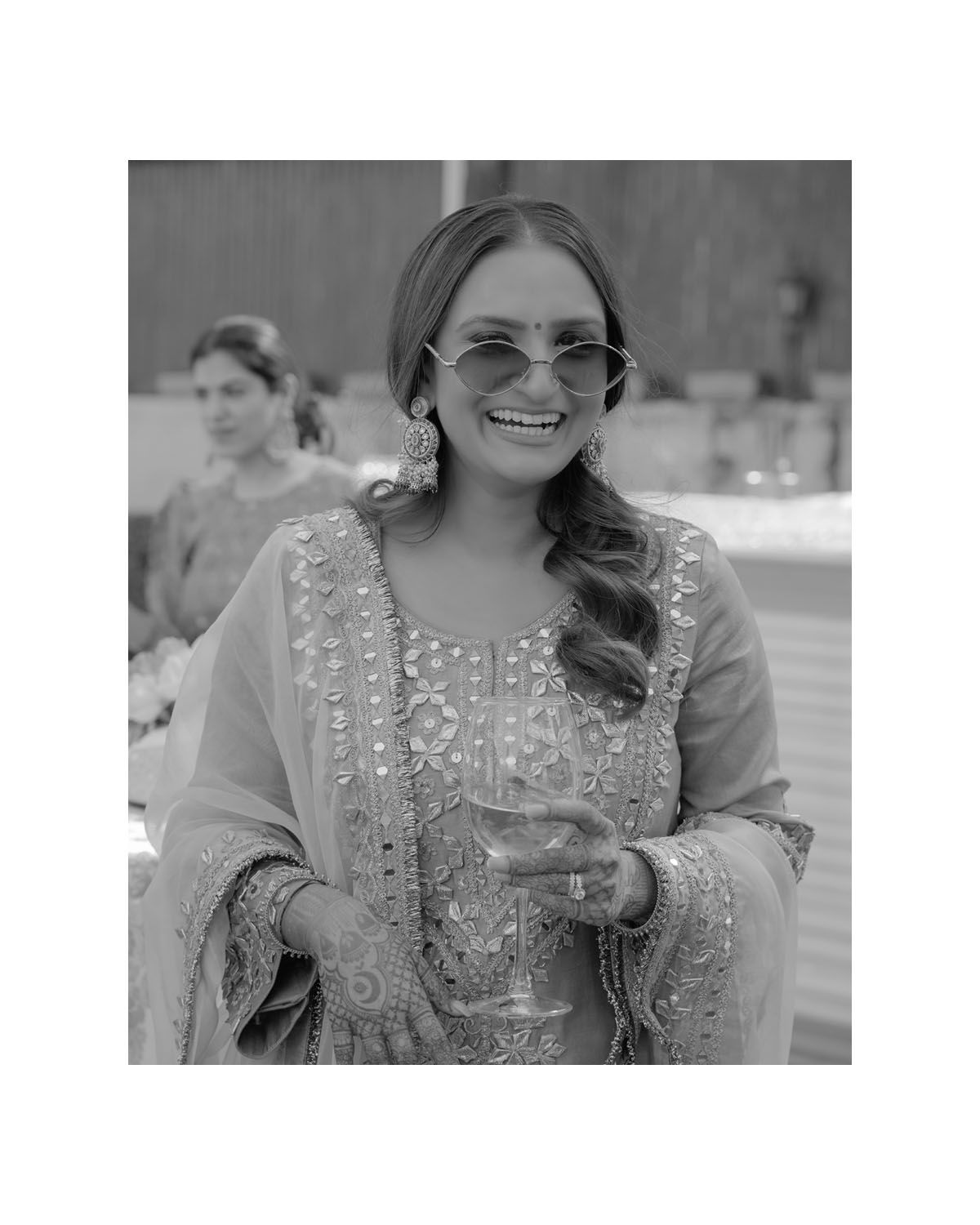 Black and white portrait of someone in formal attire holding a drink glass and wearing sunglasses.