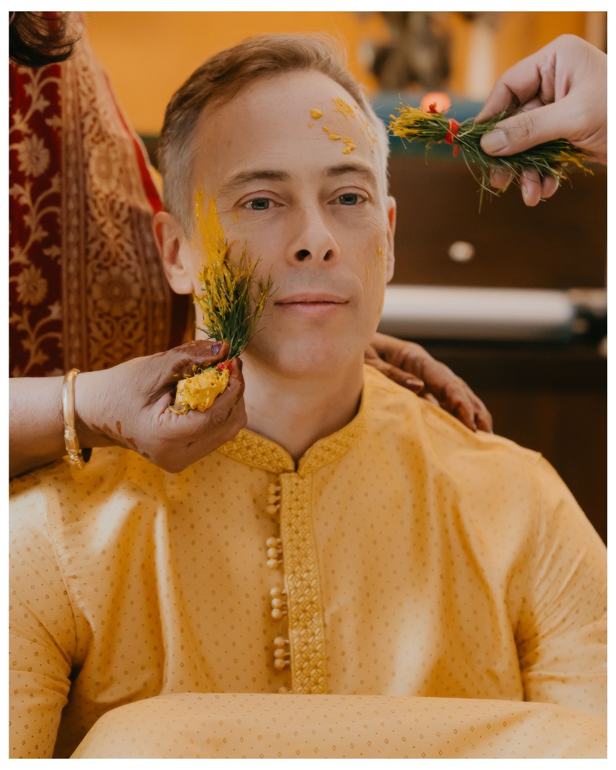 Man in yellow kurta receiving traditional turmeric application during Indian ceremony.
