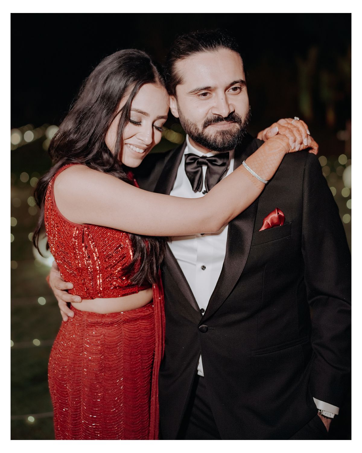 A couple shares an intimate dance moment, with the woman in a sparkling red dress and the man in a formal tuxedo.