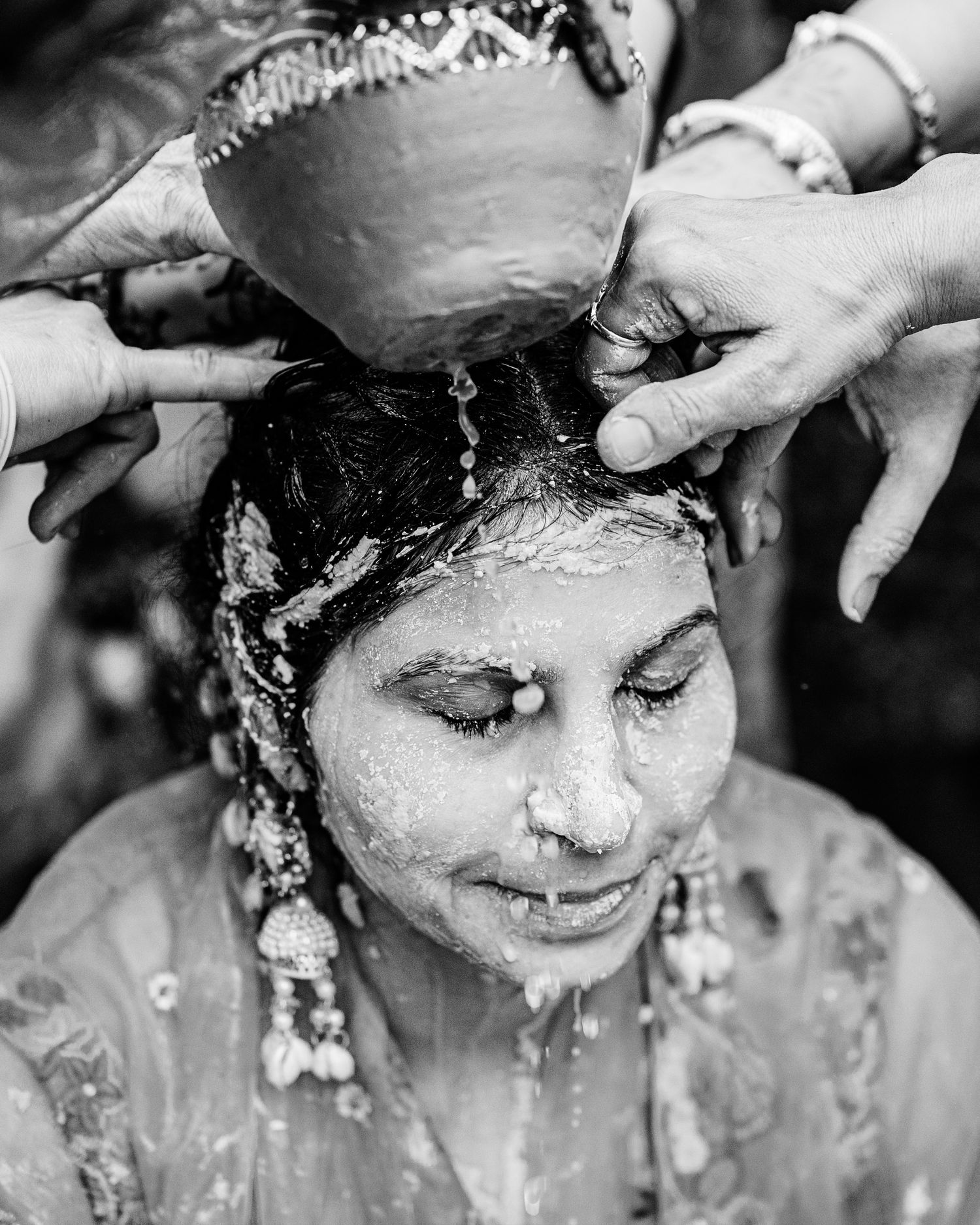 Black and white photo of a woman having water poured over her head during a traditional Hindu wedding ceremony.