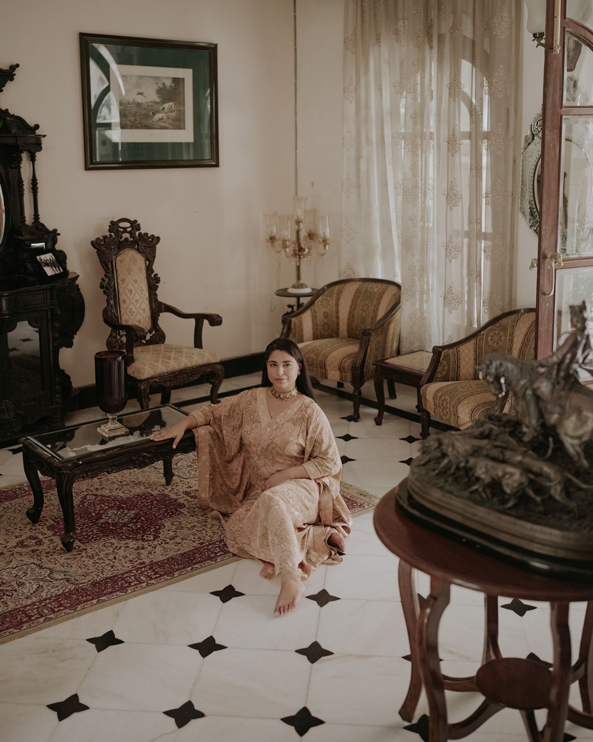 Person in flowing dress seated in an elegant vintage living room with antique furniture and ornate decor.