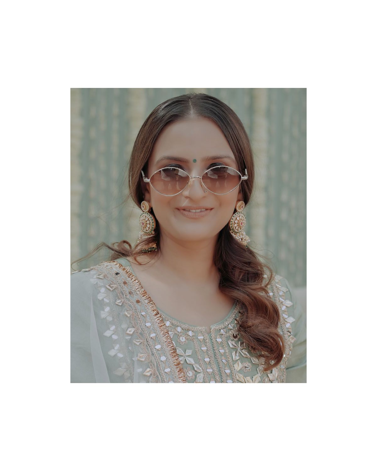 Close-up portrait showing intricate jewelry and stylish sunglasses with a soft grey background.