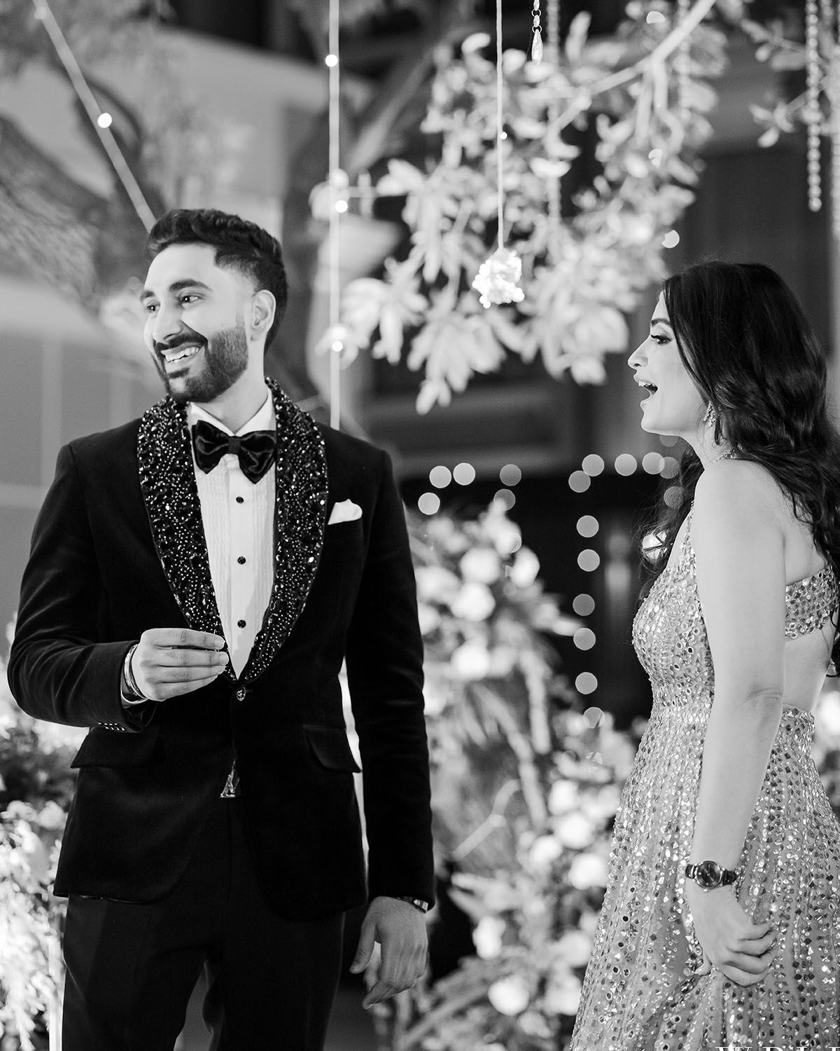 Candid black and white photo of couple laughing beneath hanging snowflake decorations.
