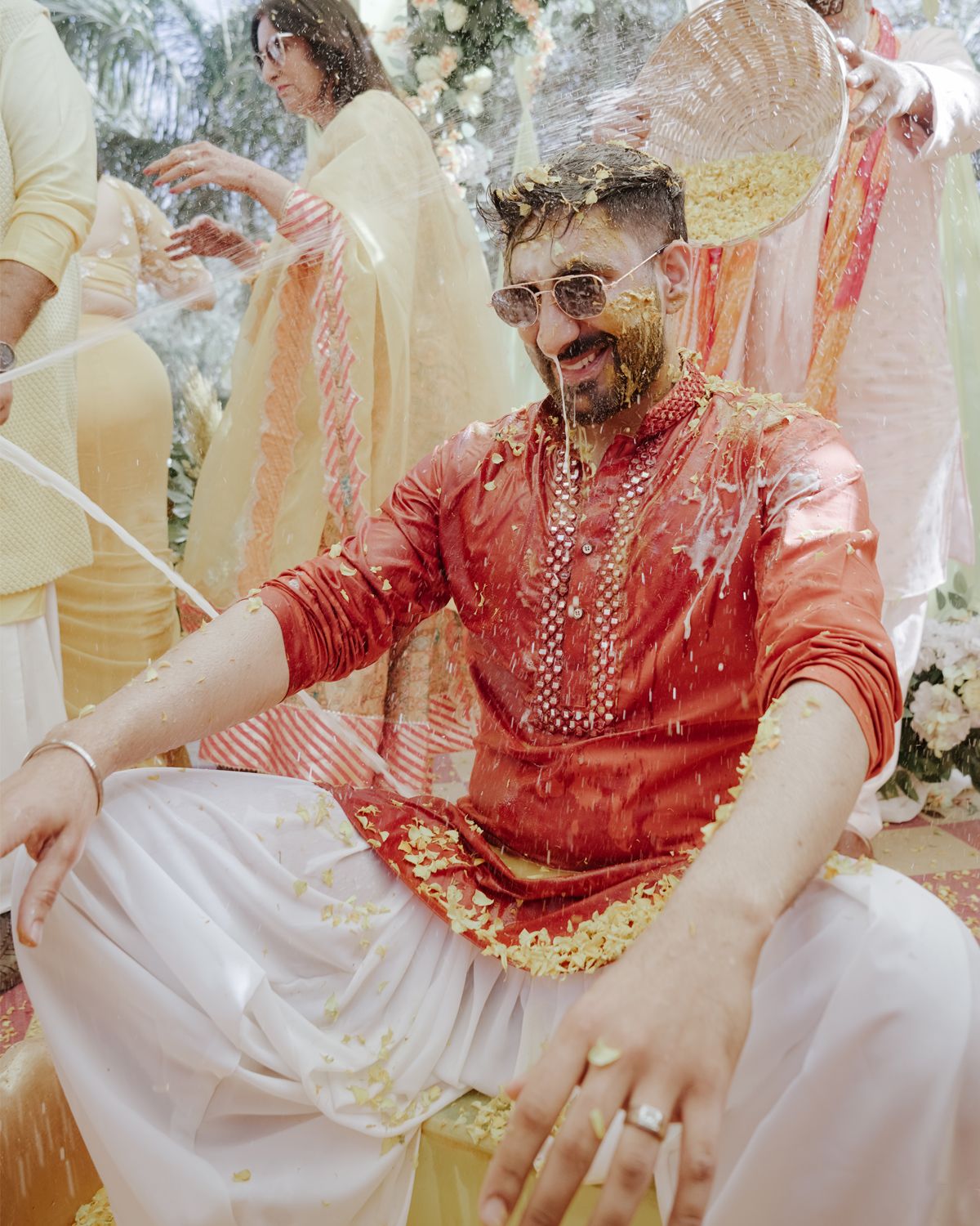 Festive celebration shows guests in traditional Indian attire with red and gold decorations.