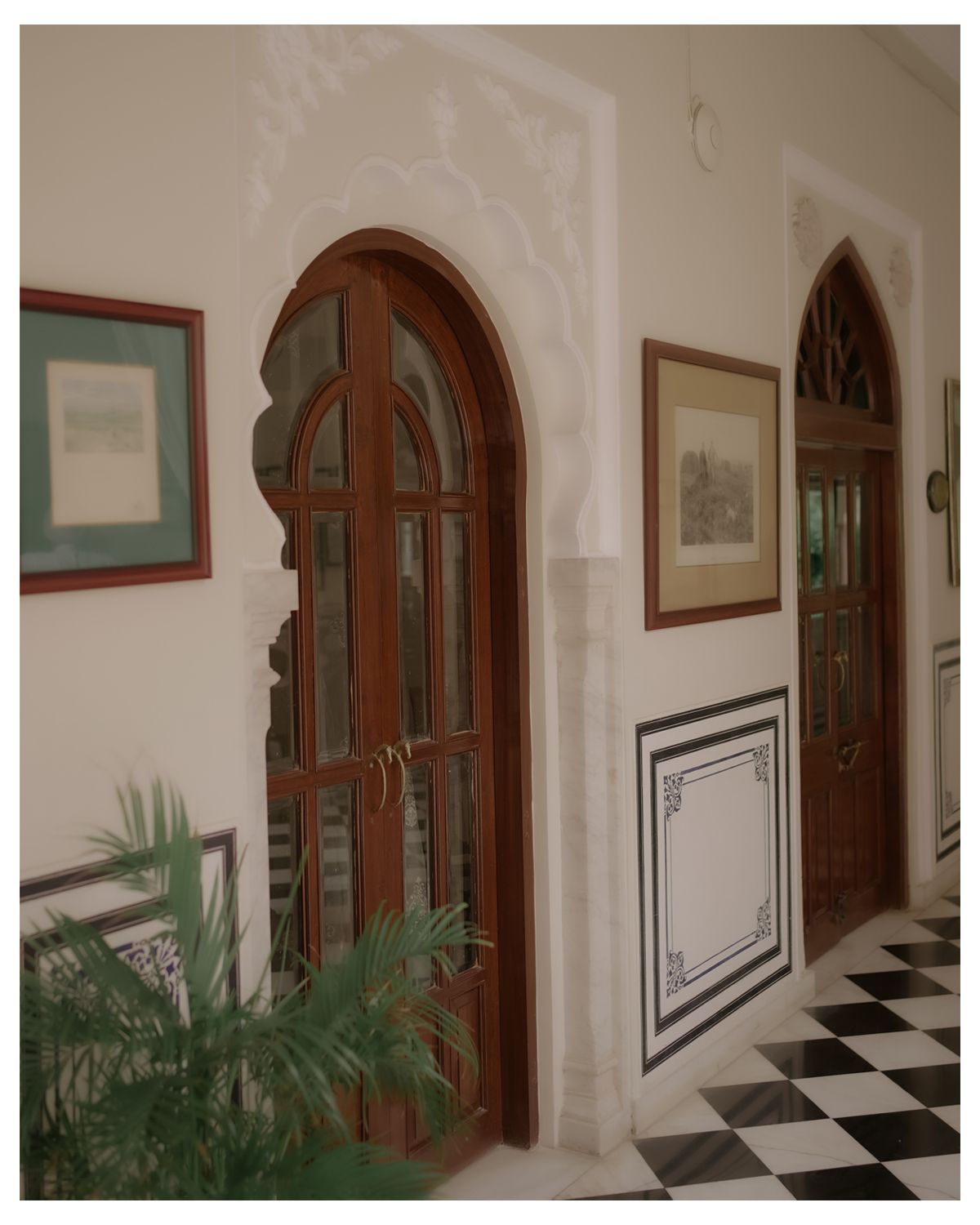 Elegant interior space with arched doorways, checkered flooring and decorative potted plants.