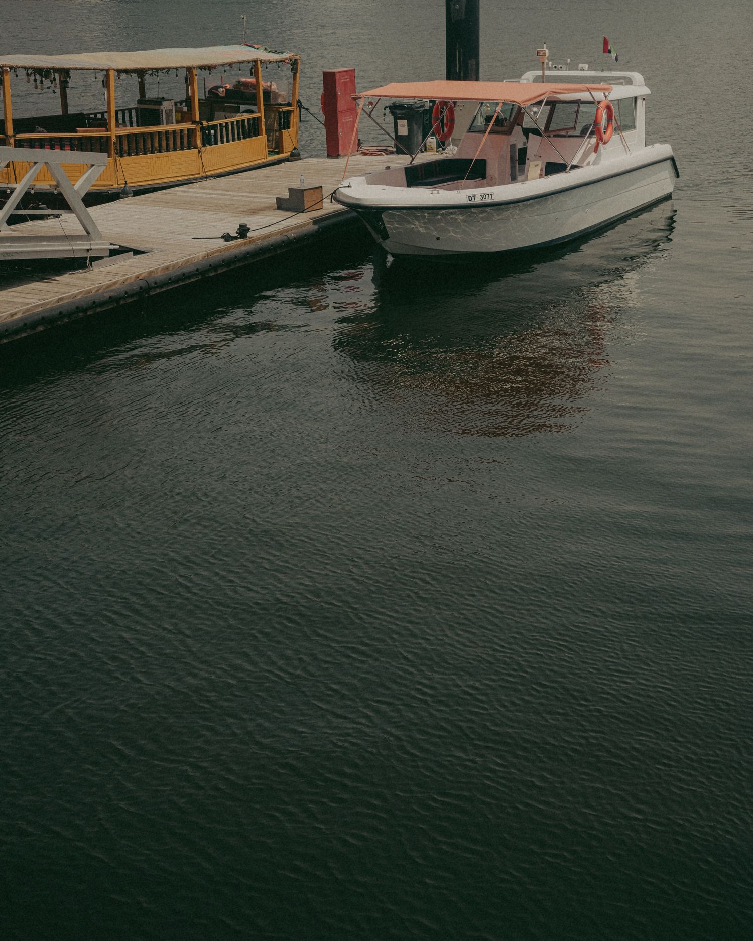 Two boats docked at a wooden pier on calm dark water, including a white motorboat and a yellow covered vessel.