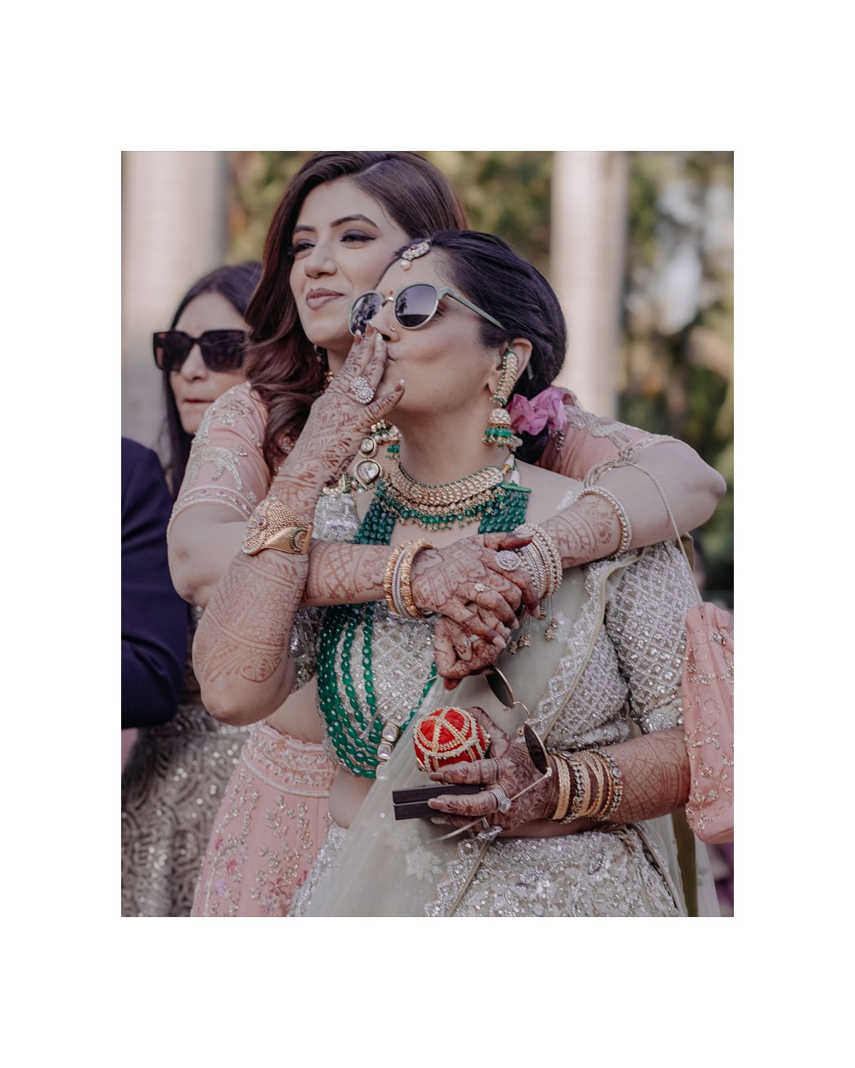 Wedding guests in traditional South Asian attire pose with drinks and jewelry at an outdoor celebration.