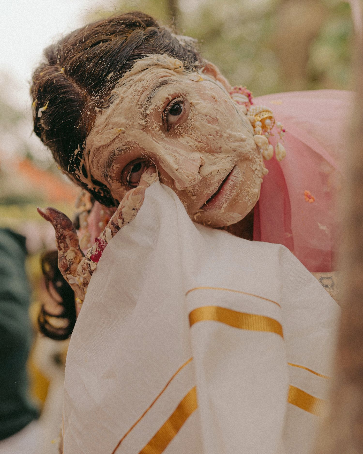 Elderly woman with haldi on face holding white and gold saree at traditional Indian ceremony.
