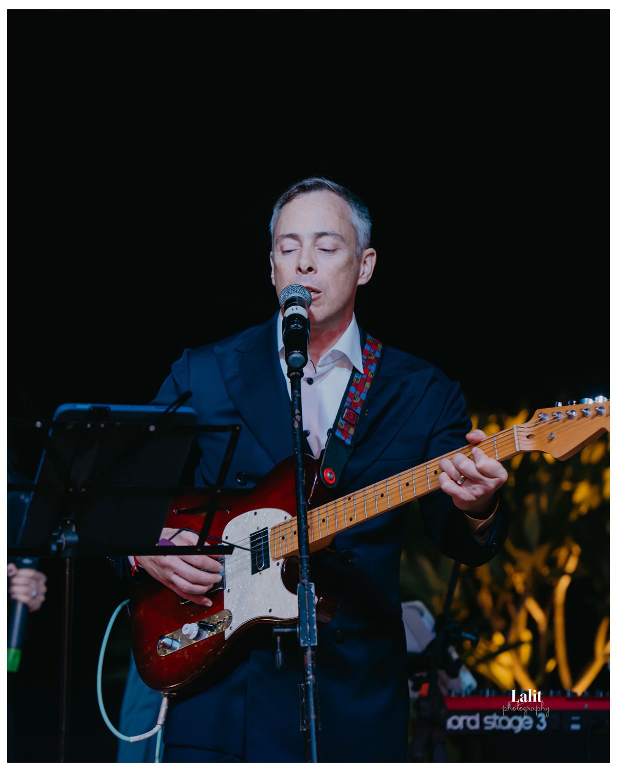 Dynamic groom performs with a red electric guitar under dramatic stage lighting.