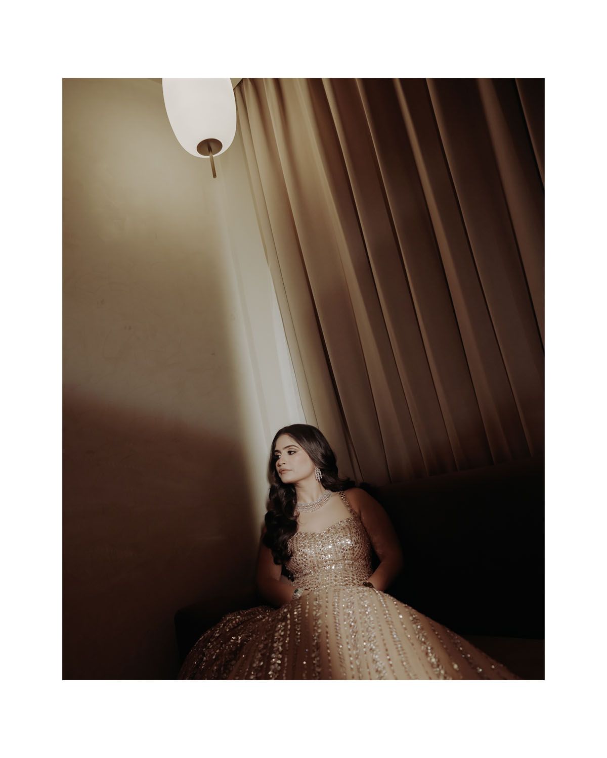 Moody portrait of person in sparkly ball gown seated under pendant light.