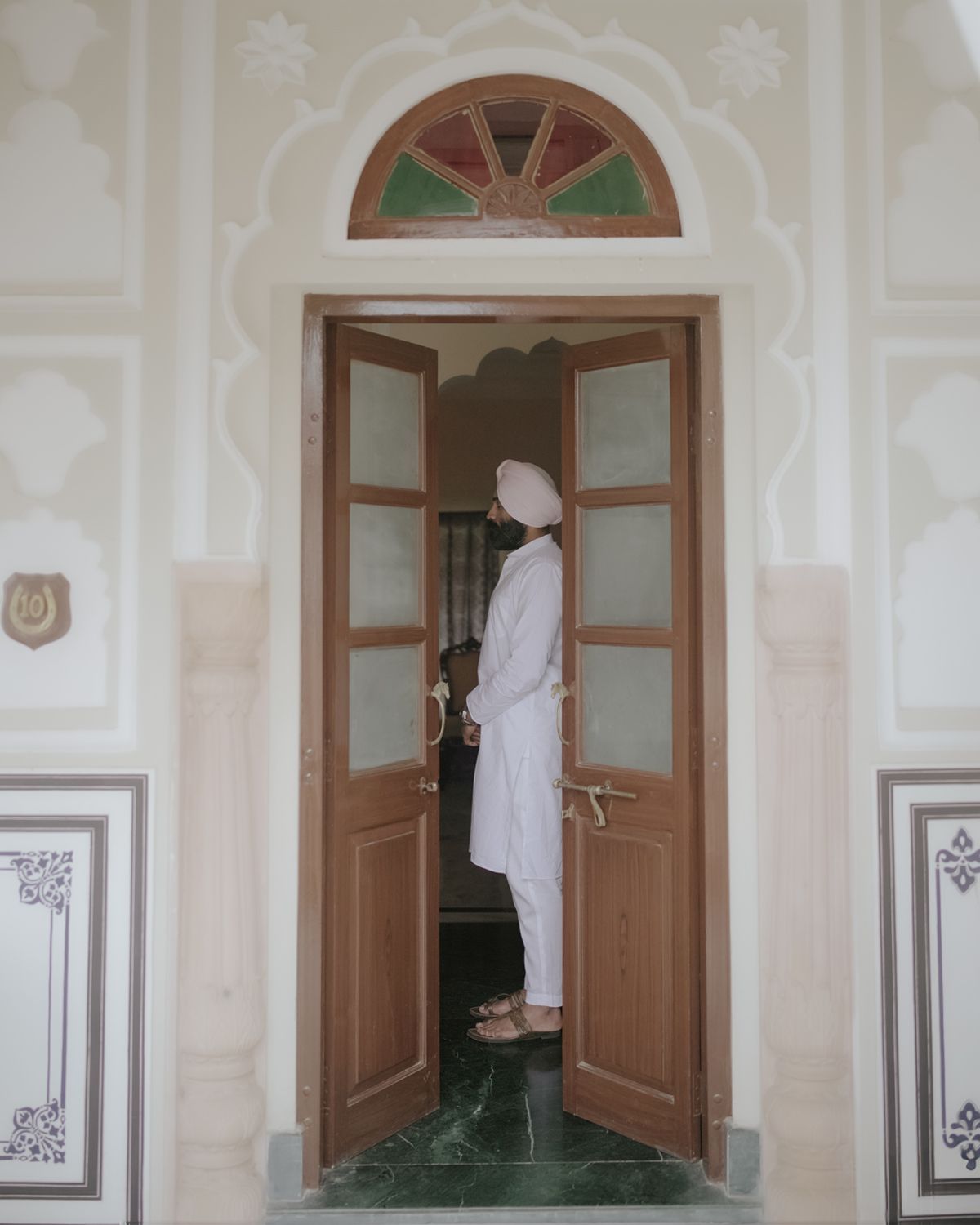 Person stands in ornate doorway with decorative arch and stained glass detail.