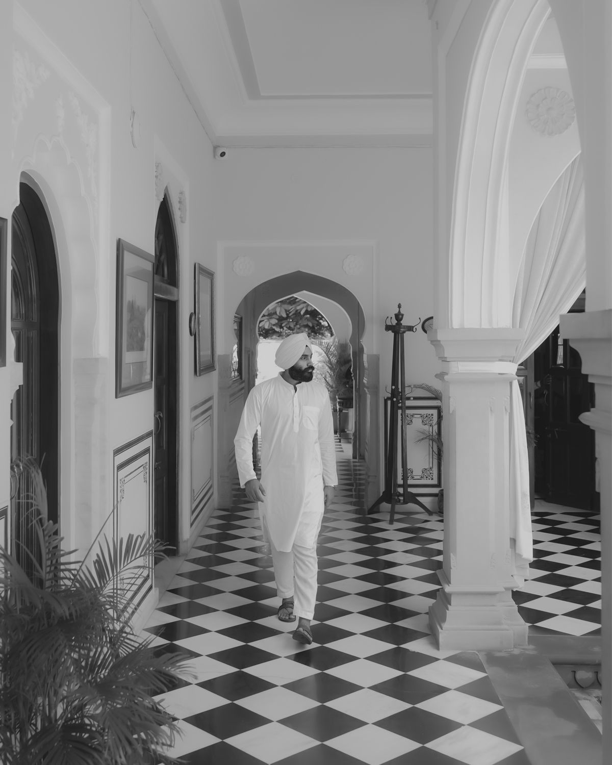 Figure in white walks through elegant hallway with checkered floor and arched doorways.