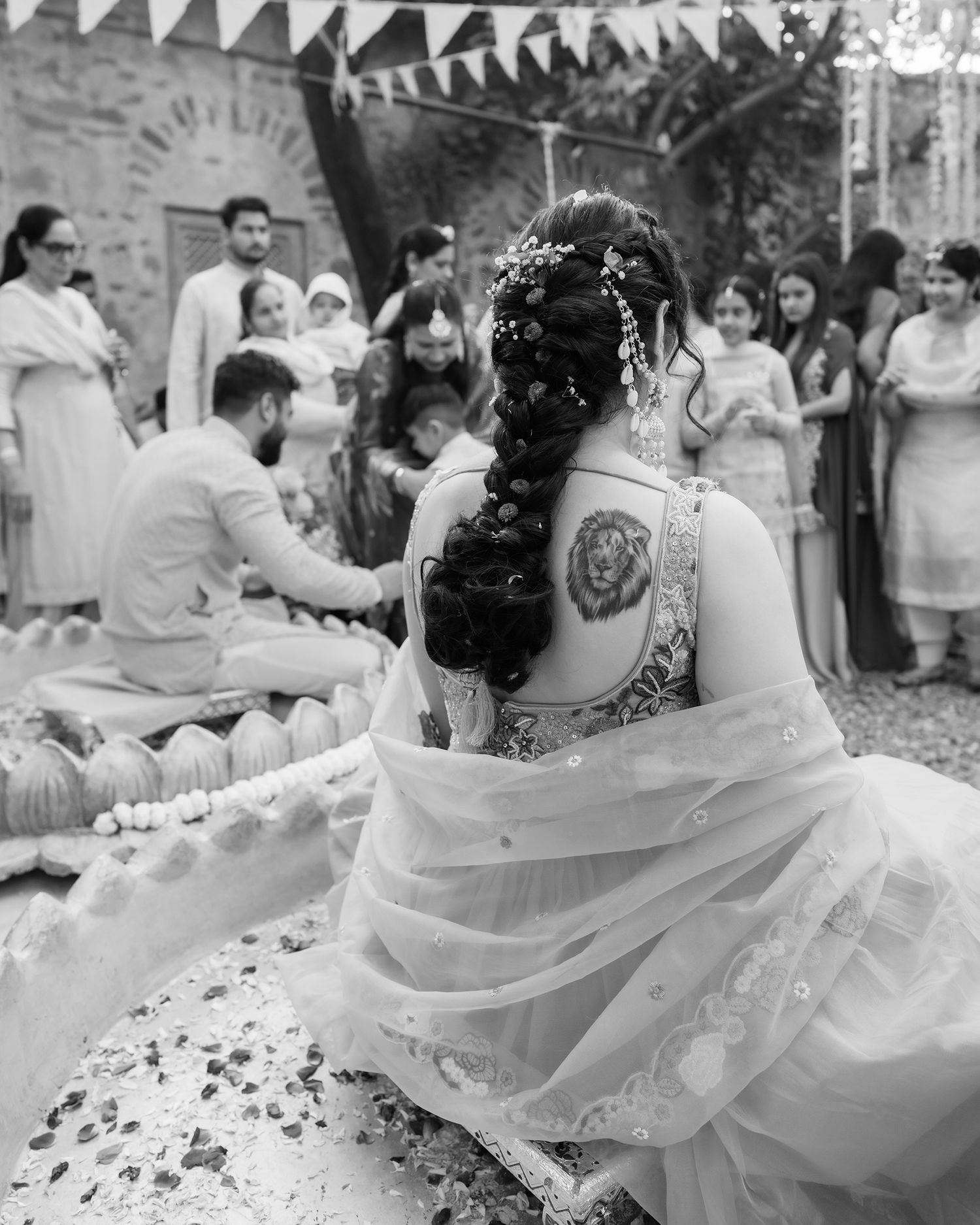 Black and white photo of bride with braided hair and back tattoo during traditional Indian wedding ceremony.