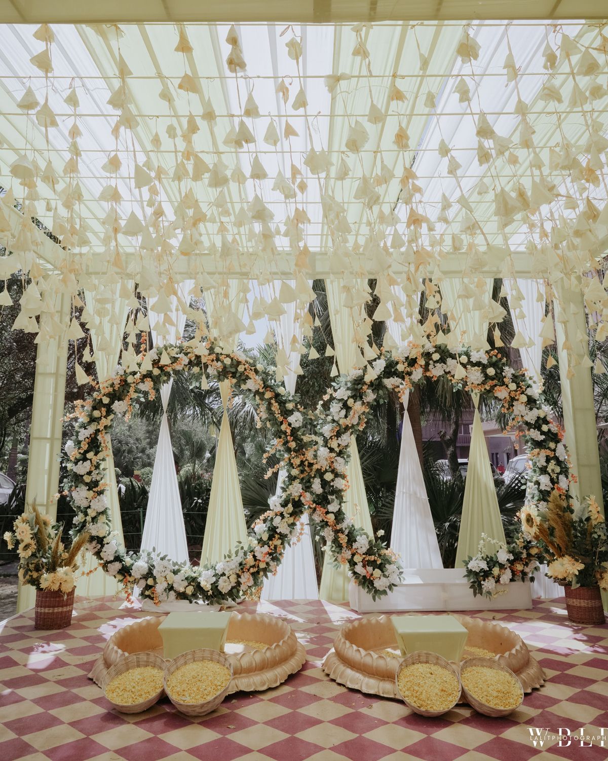 Wedding decoration with floral arches and hanging lights over outdoor seating area.