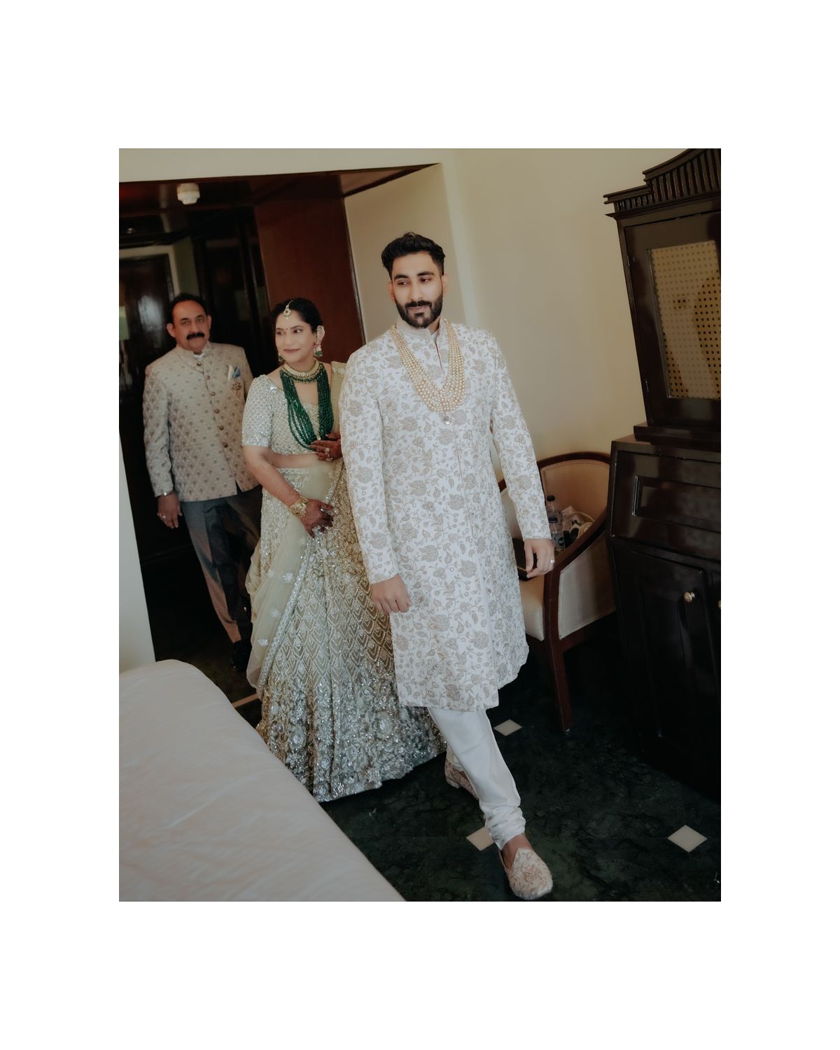 People in traditional Indian formal wear walk through an elegant indoor setting.