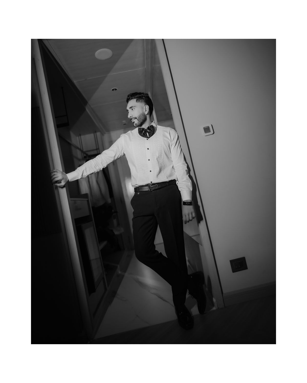 Artistic black and white portrait of person in white dress shirt and black pants leaning against a wall.