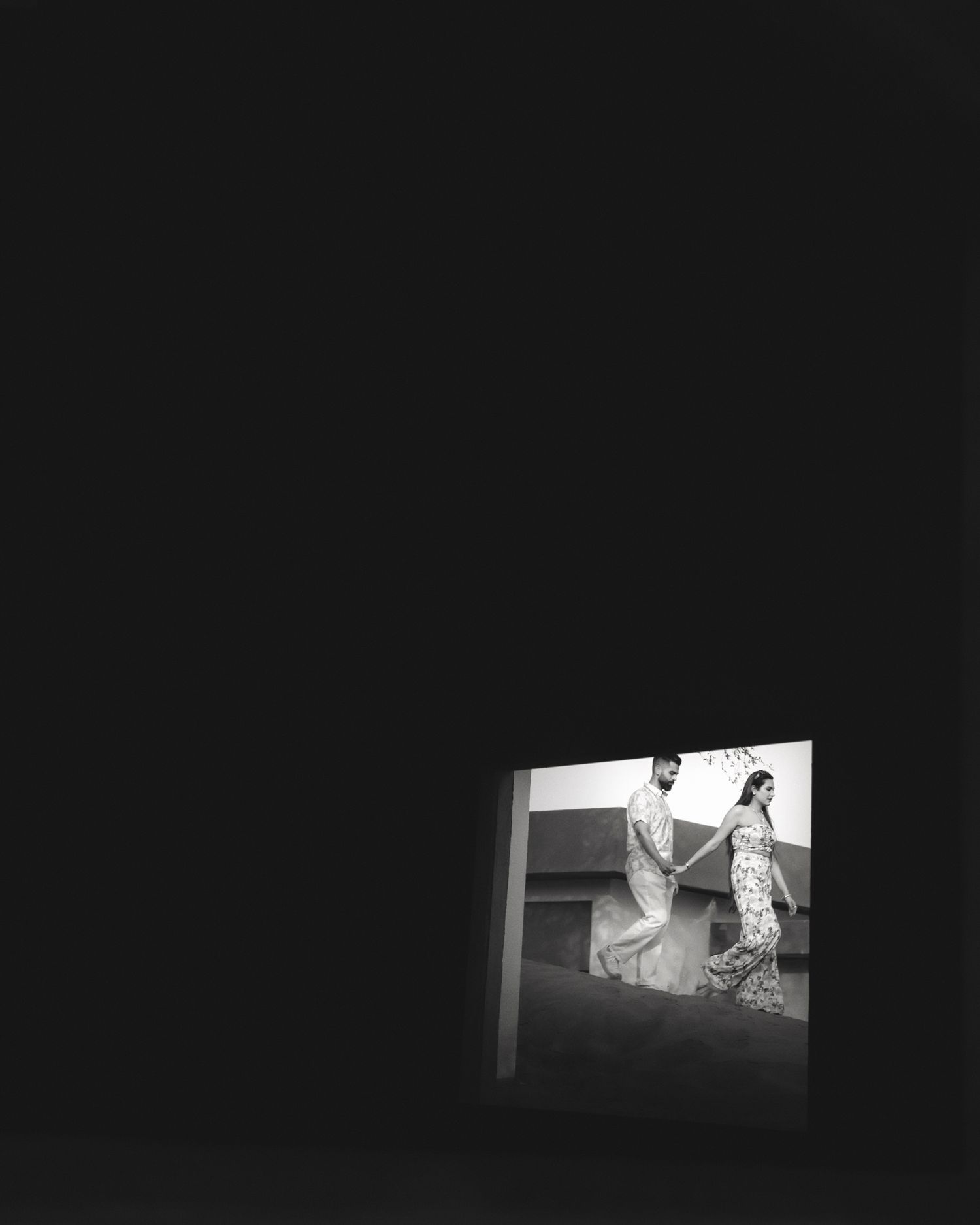 Black and white photo of two people in traditional attire viewed through a small window against a dark background.