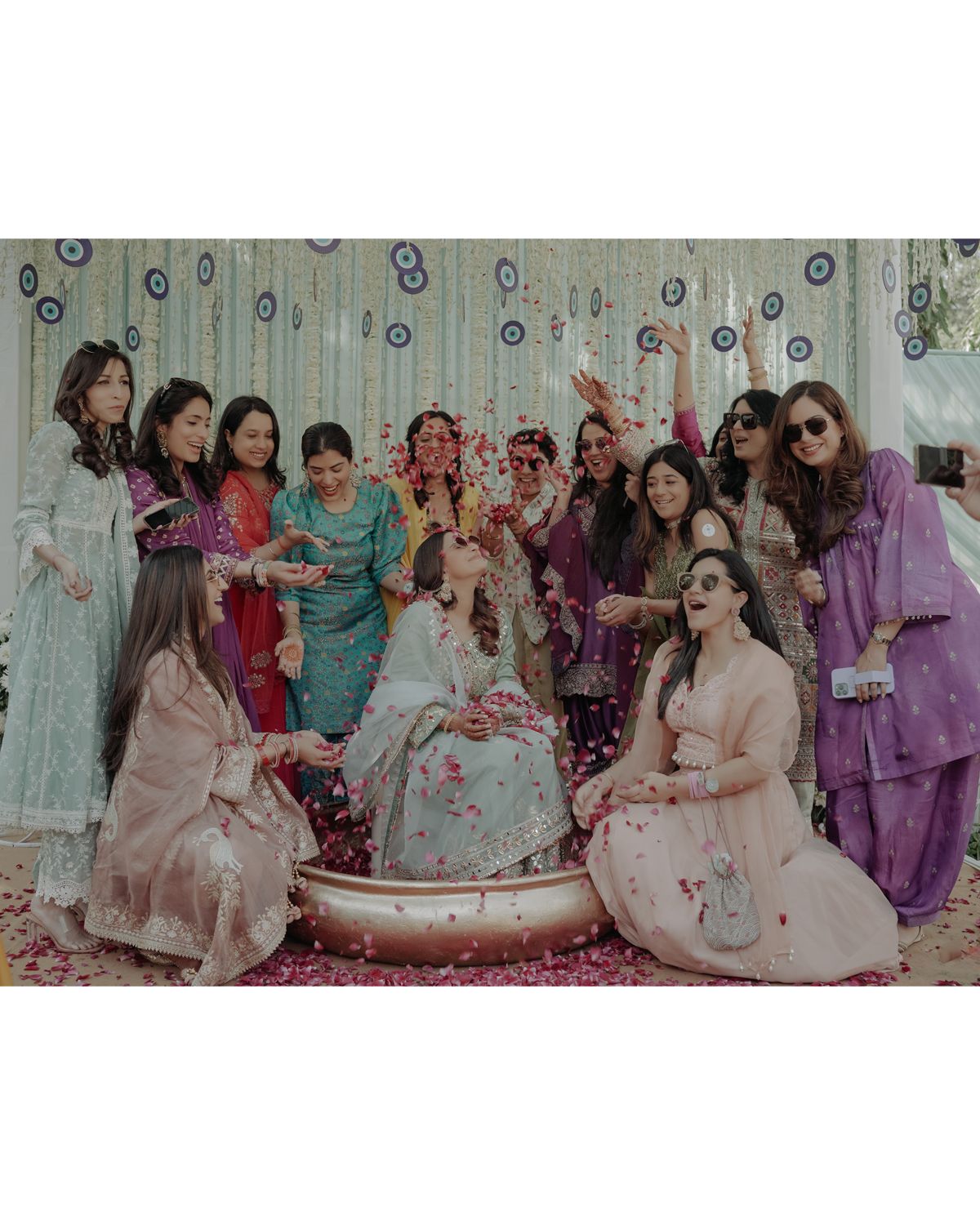 Group celebration with bride in white dress surrounded by friends throwing pink rose petals.