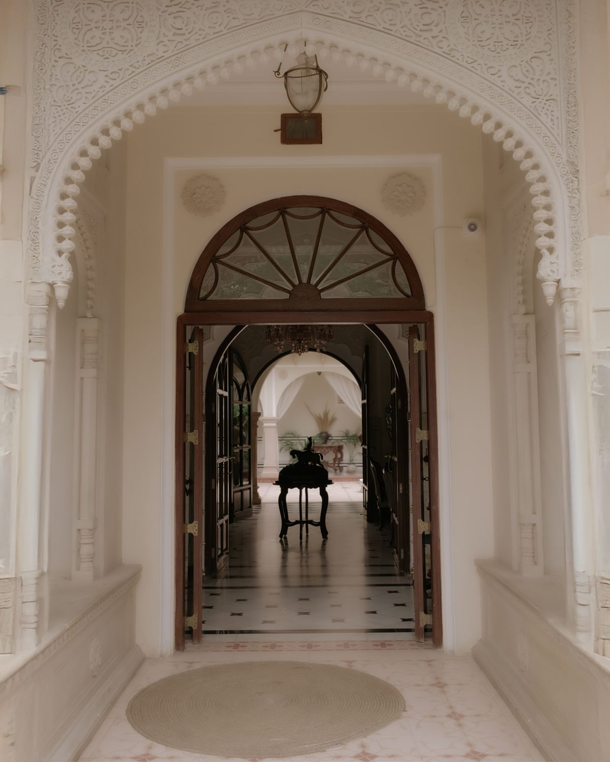 An elegant white marble hallway with ornate arched doorway and decorative ceiling details.