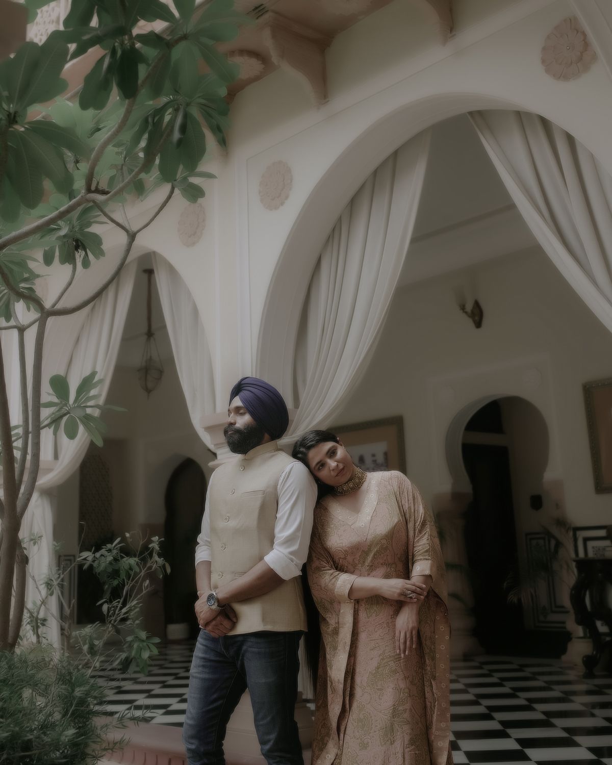 Couple standing under ornate white archways with checkered floor and indoor plants.