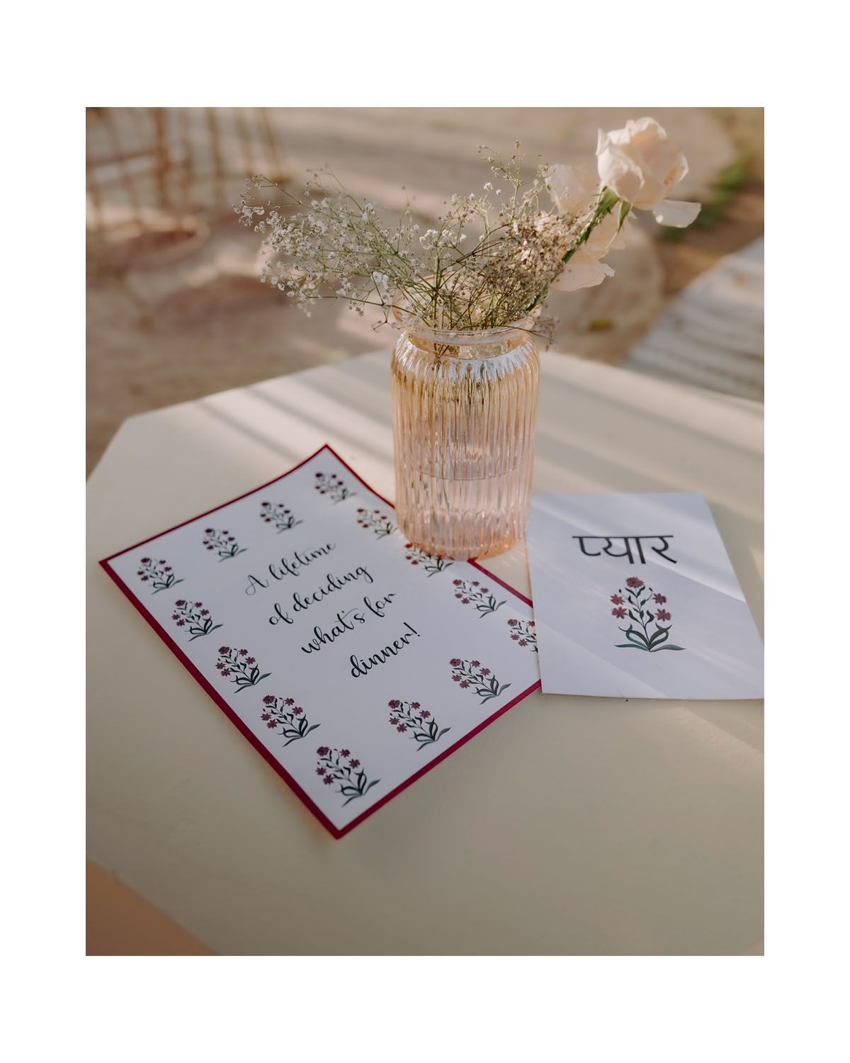 A glass vase with a delicate flower and handwritten cards with floral designs sit on a light colored surface.