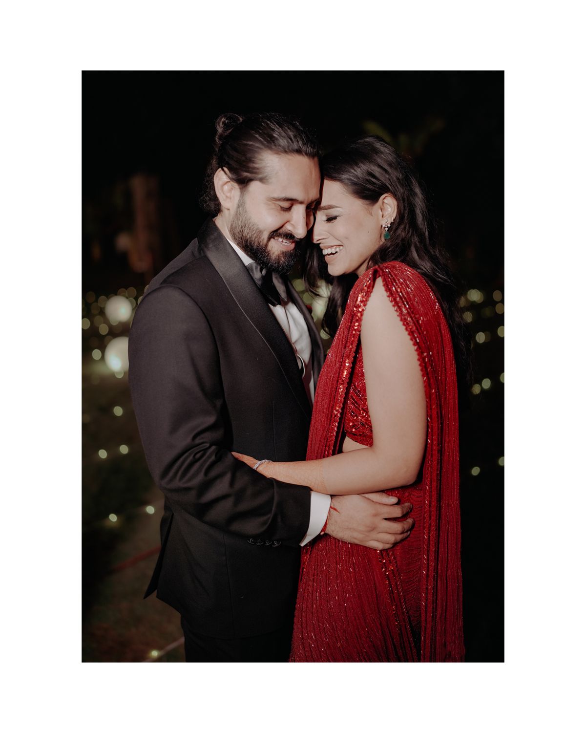 A couple embraces intimately at night, with a person wearing a red flowing dress and another in a dark suit in moody lighting.