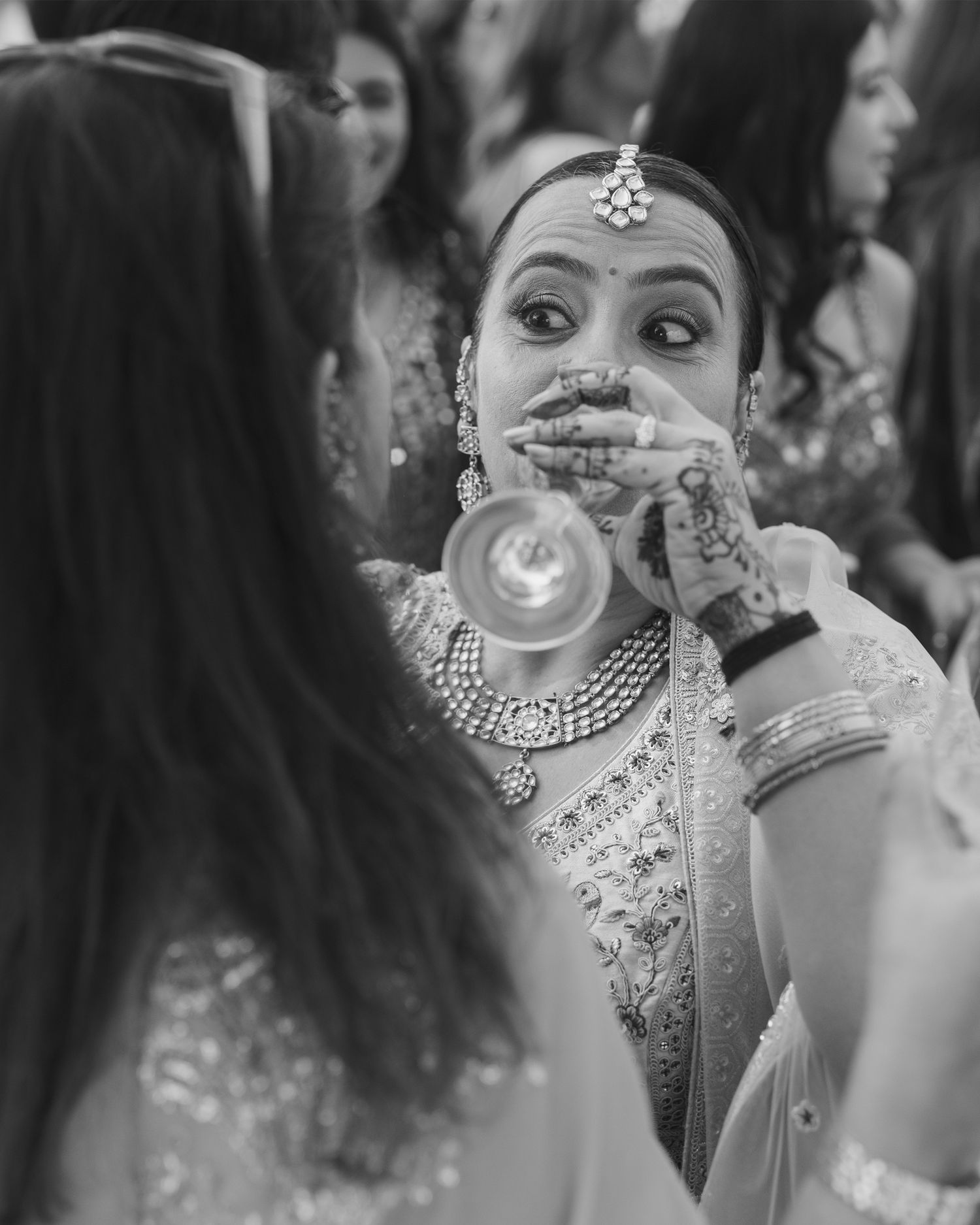 Black and white photo of an Indian bride in traditional jewelry and mehndi holding a diya during wedding ceremony.