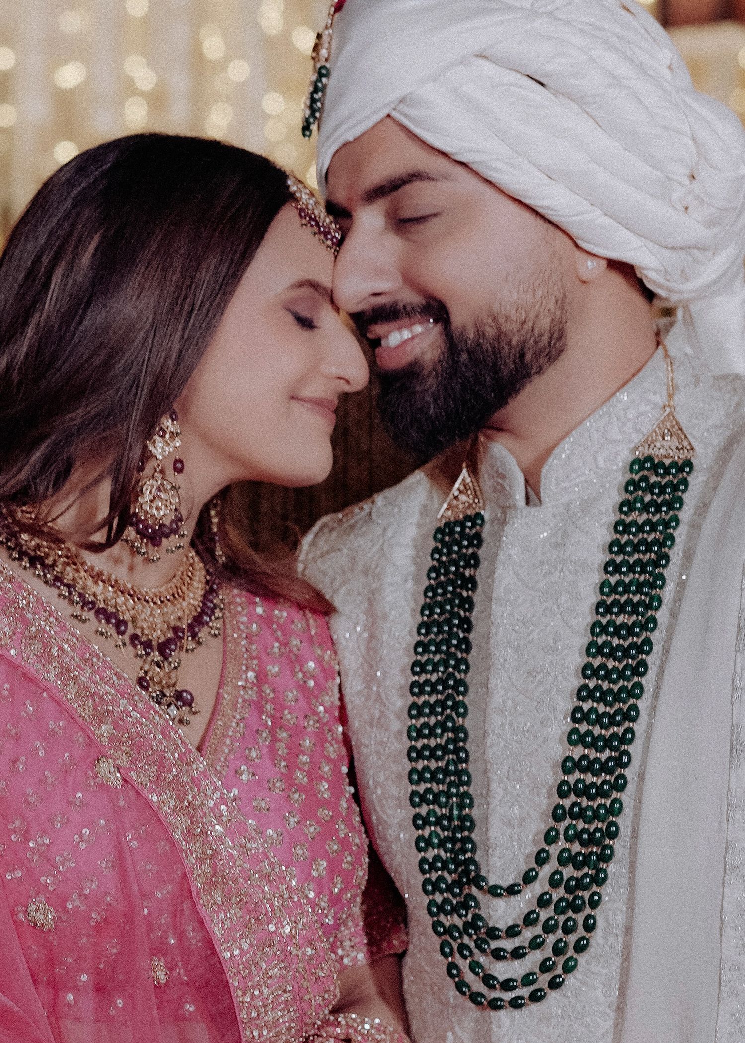 A romantic couple in traditional Indian wedding attire sharing an intimate moment wearing ornate jewelry and traditional dress.
