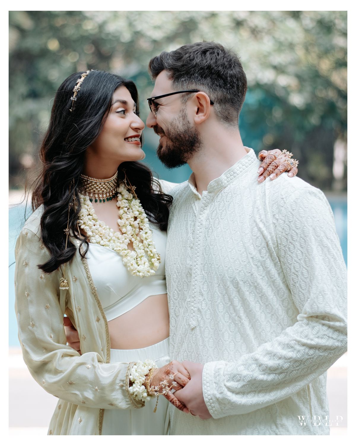 Couple wearing matching white outfits share a romantic moment during their Indian wedding celebration.