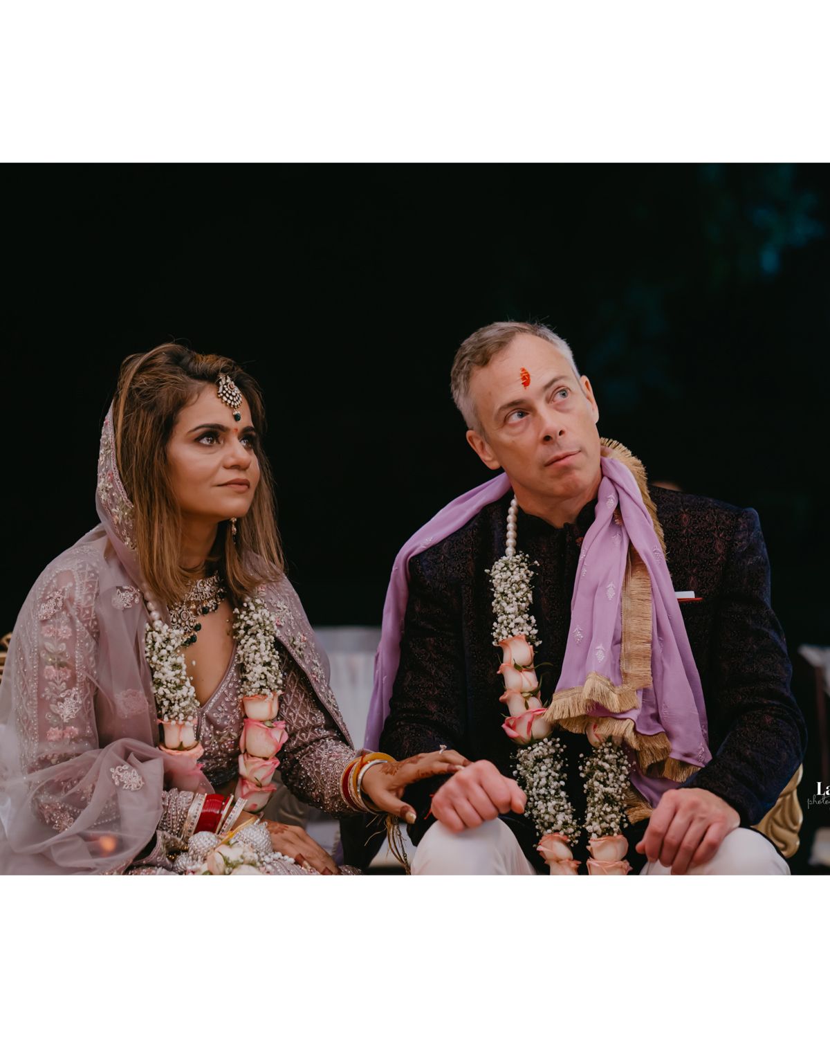 Couple in traditional Indian wedding attire with floral garlands during ceremony.