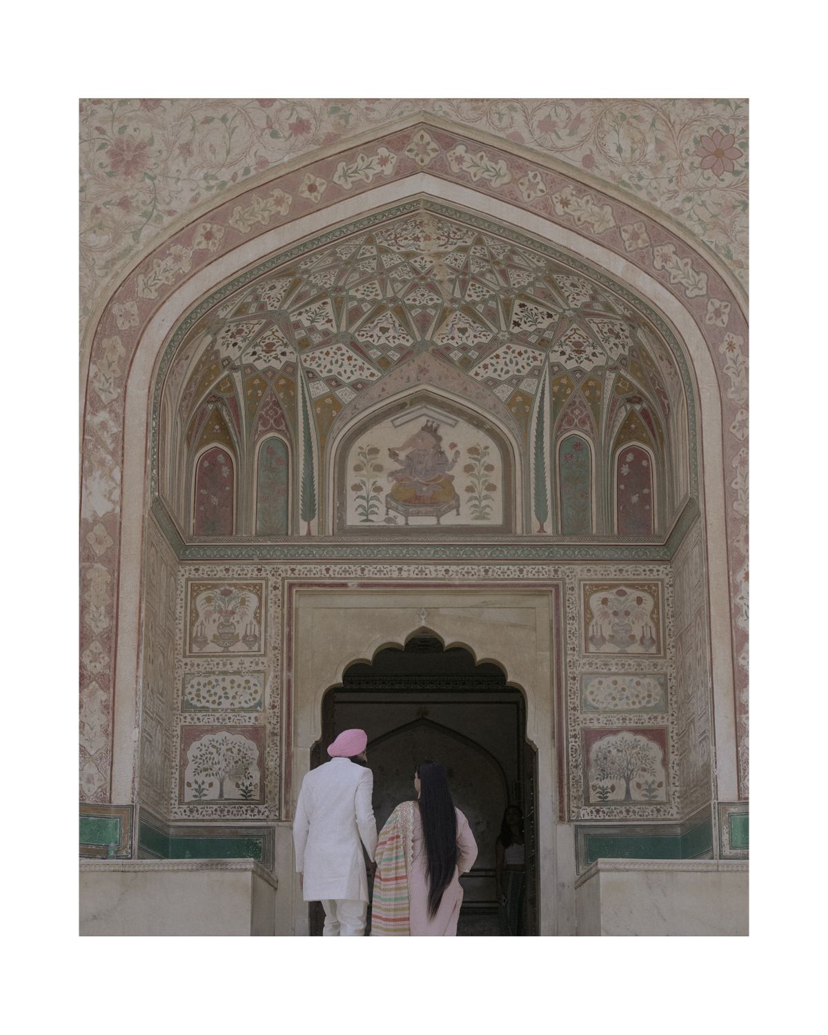 Two figures ascending steps beneath an ornately decorated Islamic architectural archway with detailed patterns.