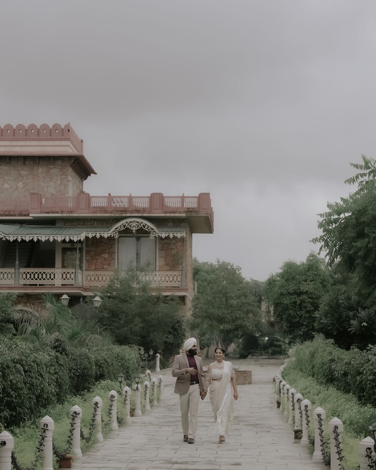 Couple walking along stone path towards historic colonial-style building on cloudy day.