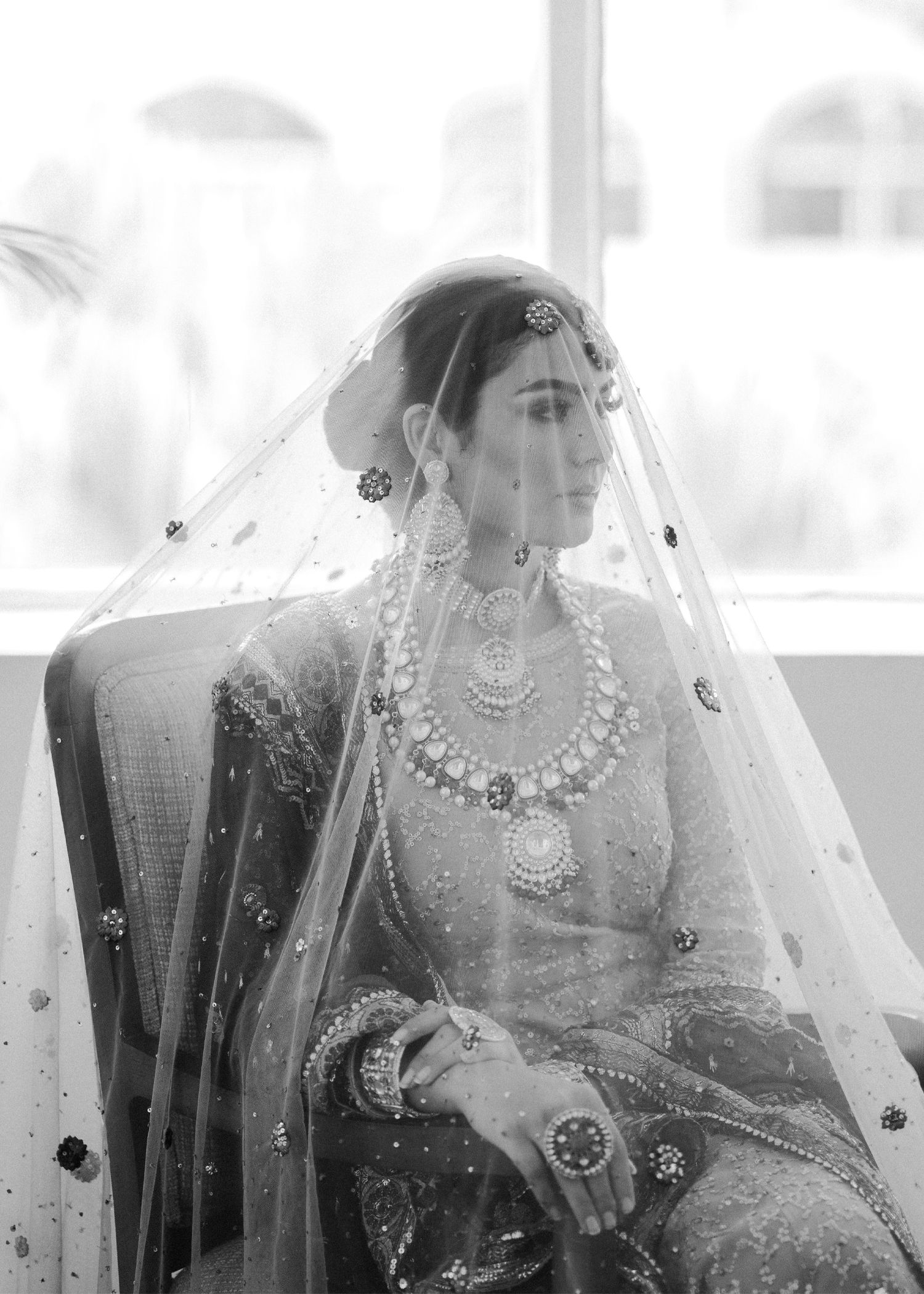 Black and white artistic wedding photo showing bride in traditional attire with henna designs and jewelry.