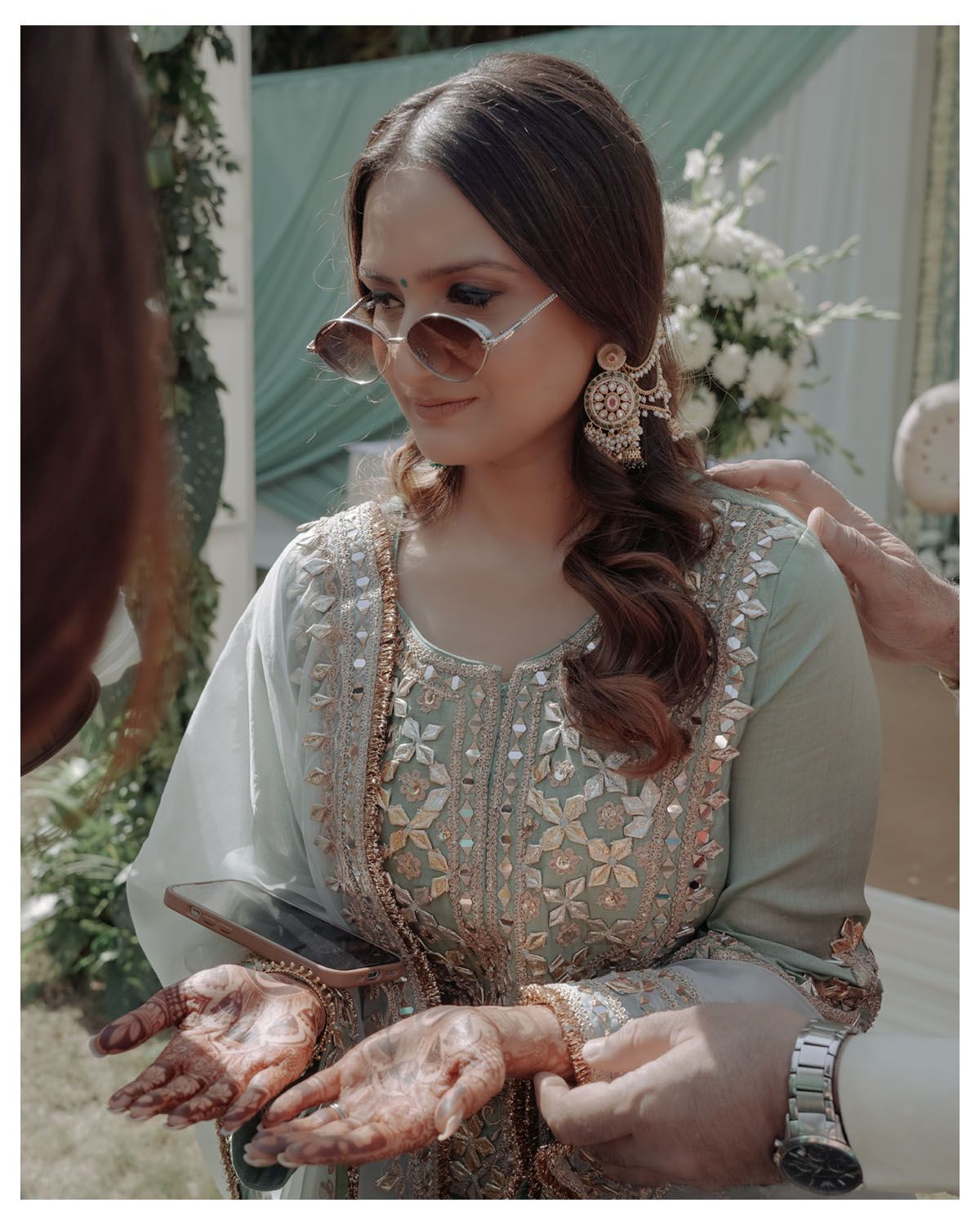Person displaying traditional henna designs on hands while wearing elegant grey embroidered outfit.
