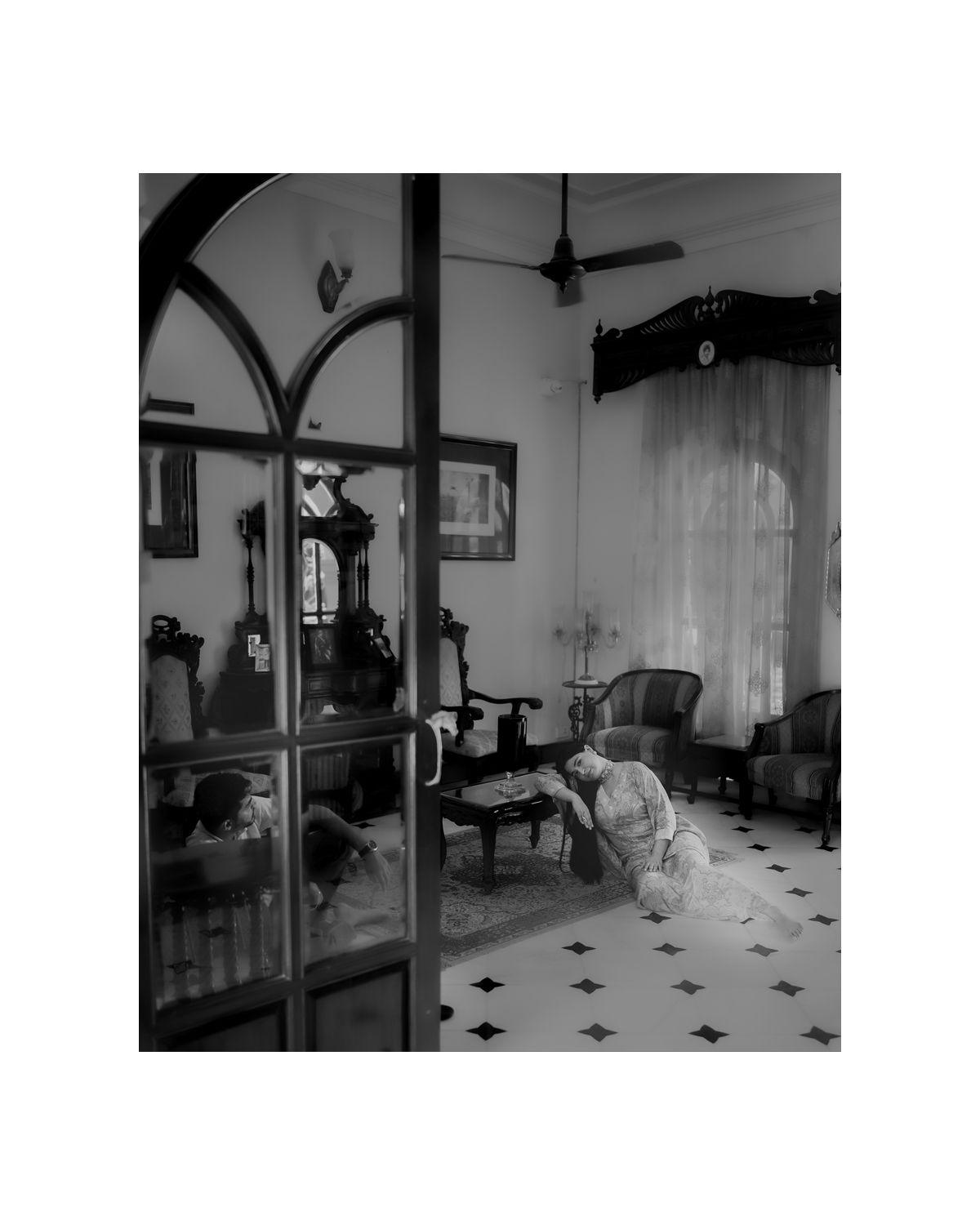 Black and white photo of vintage living room interior with person reclining among classic furniture.