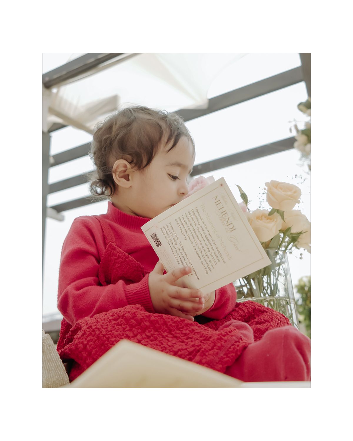 Young child in red sweater reading book while sitting outdoors.