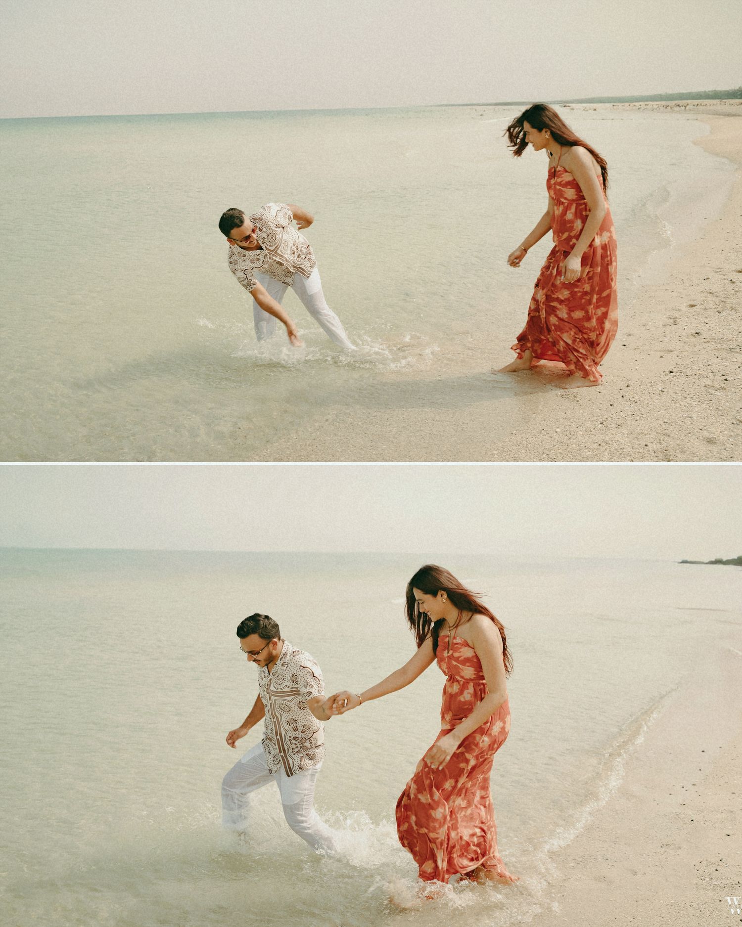 Couple playing in shallow ocean waves on a sandy beach, woman in red floral dress and man in white pants.