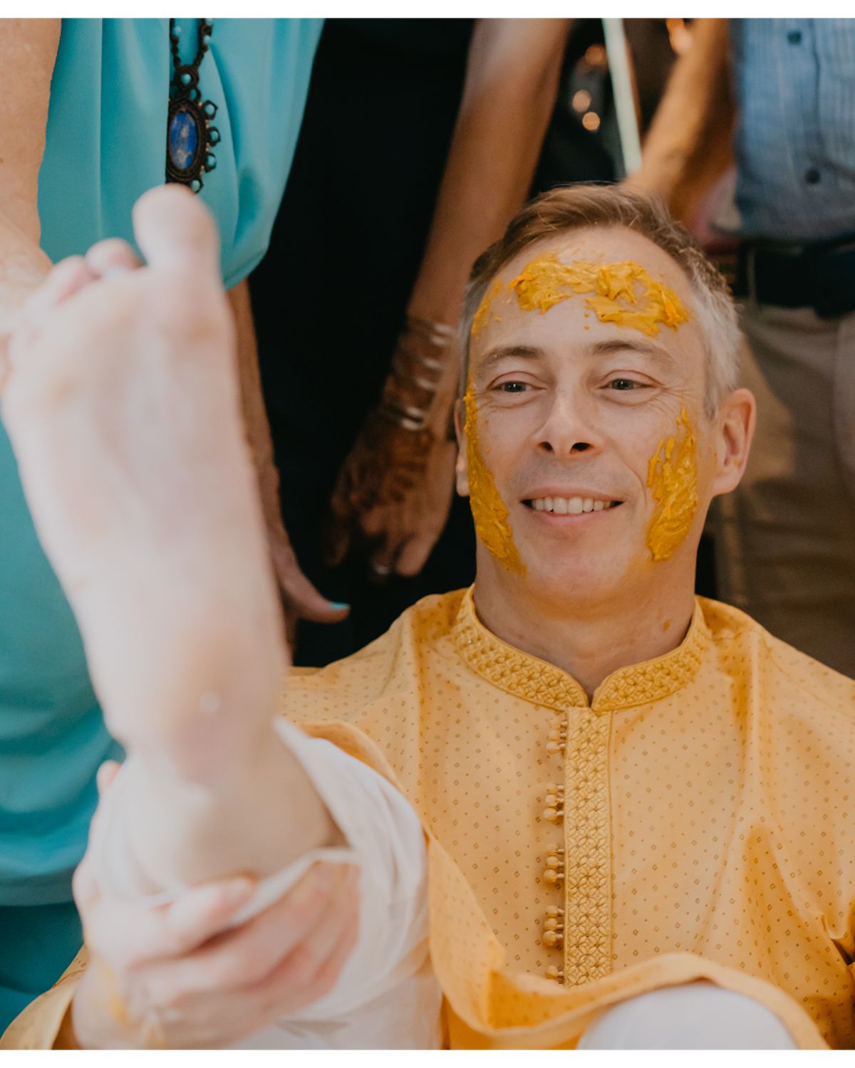 Cultural ceremony participant wearing yellow kurta receives turmeric application.