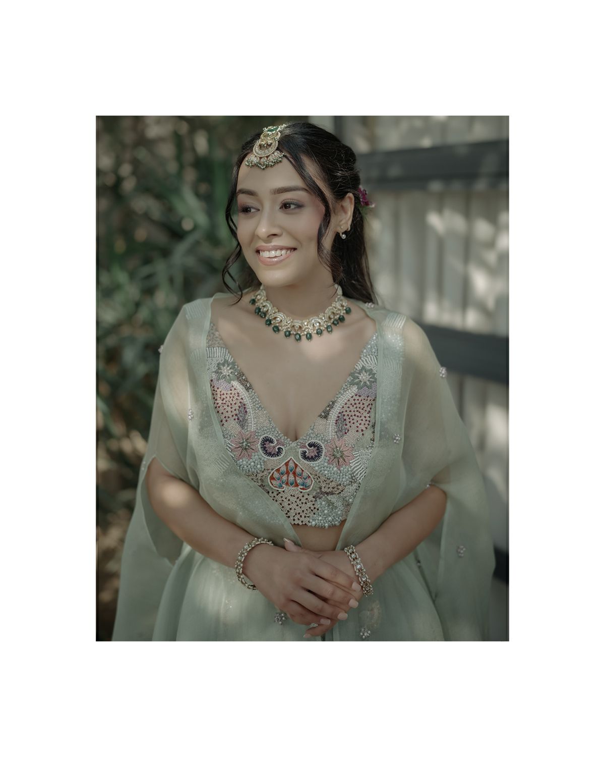 Portrait of person in mint green traditional outfit with ornate jewelry and embroidered details.