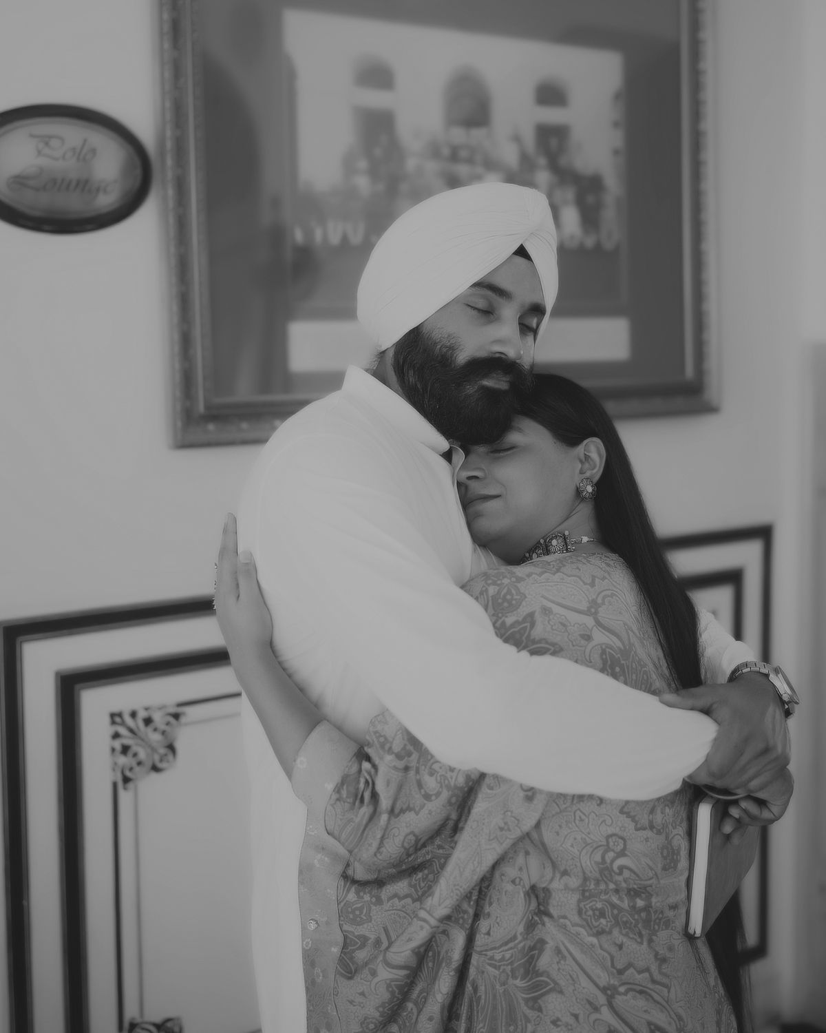 Black and white portrait capturing an intimate moment in a traditionally decorated interior space.