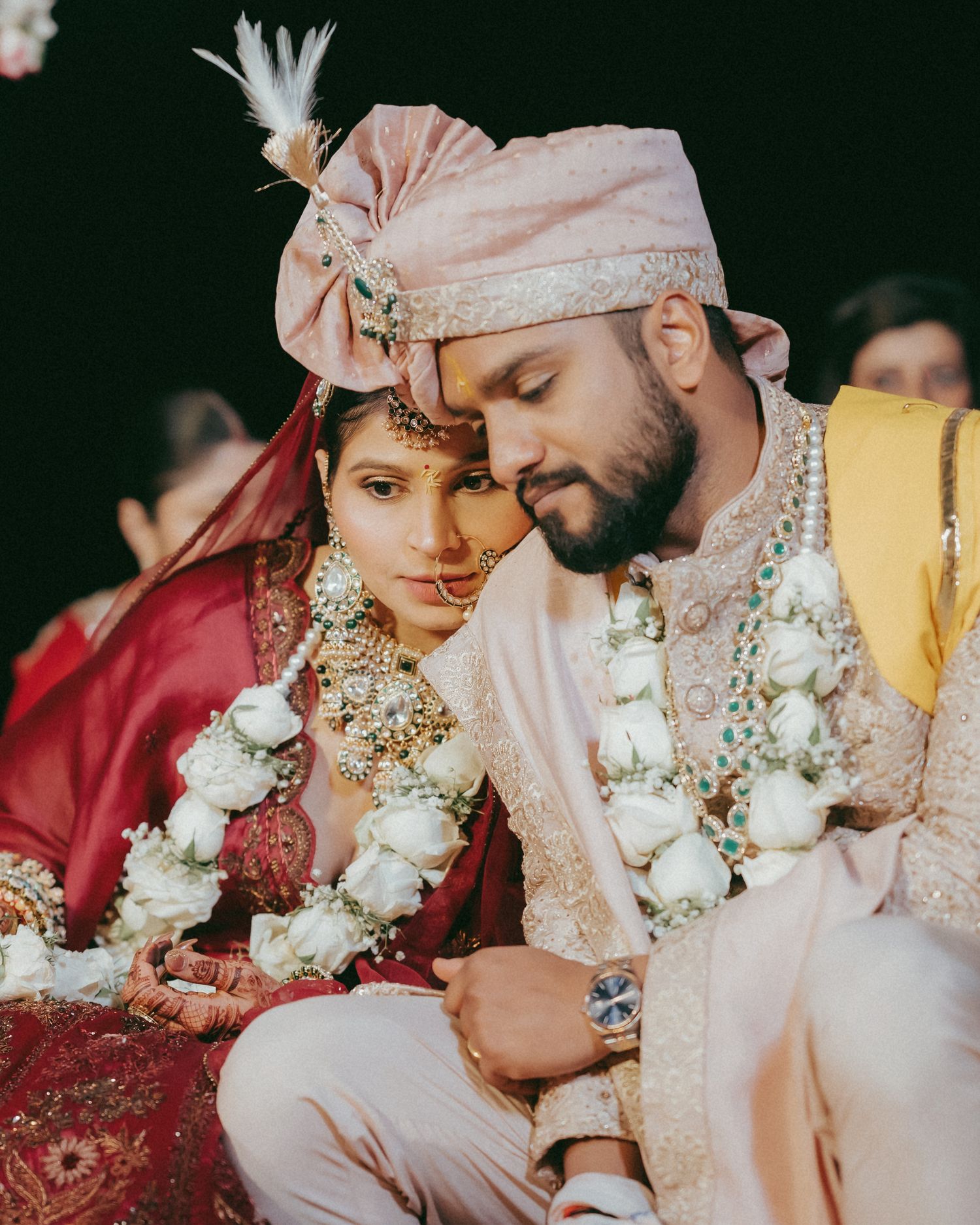 Indian bride and groom in traditional wedding attire with floral garlands sharing an intimate moment during Hindu ceremony.