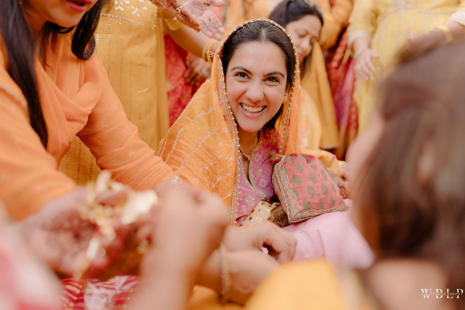 Smiling bride in yellow dupatta and pink outfit during a traditional South Asian wedding ceremony.