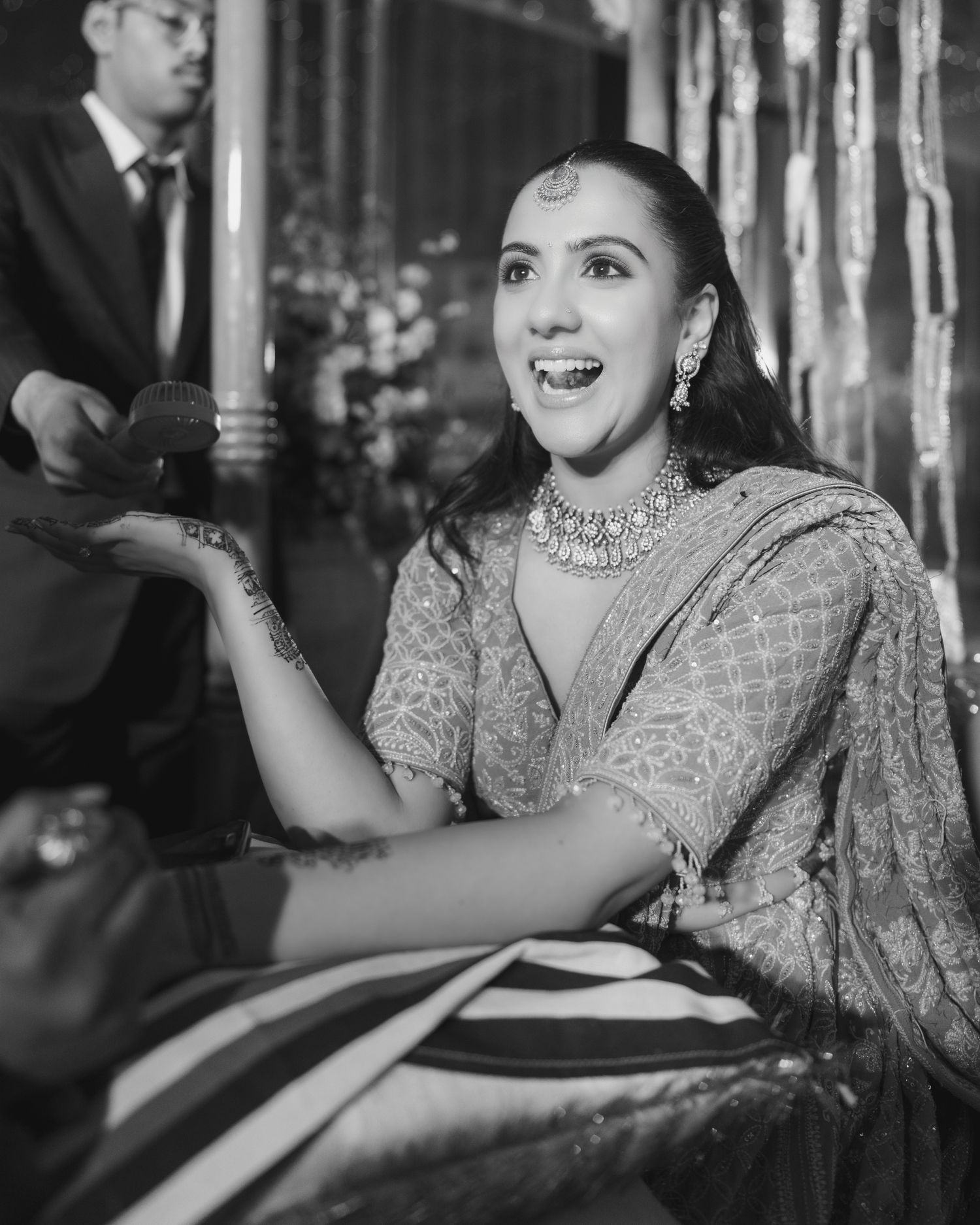 Black and white photo of a bride in traditional Indian attire with henna and diamond jewelry, smiling joyfully.